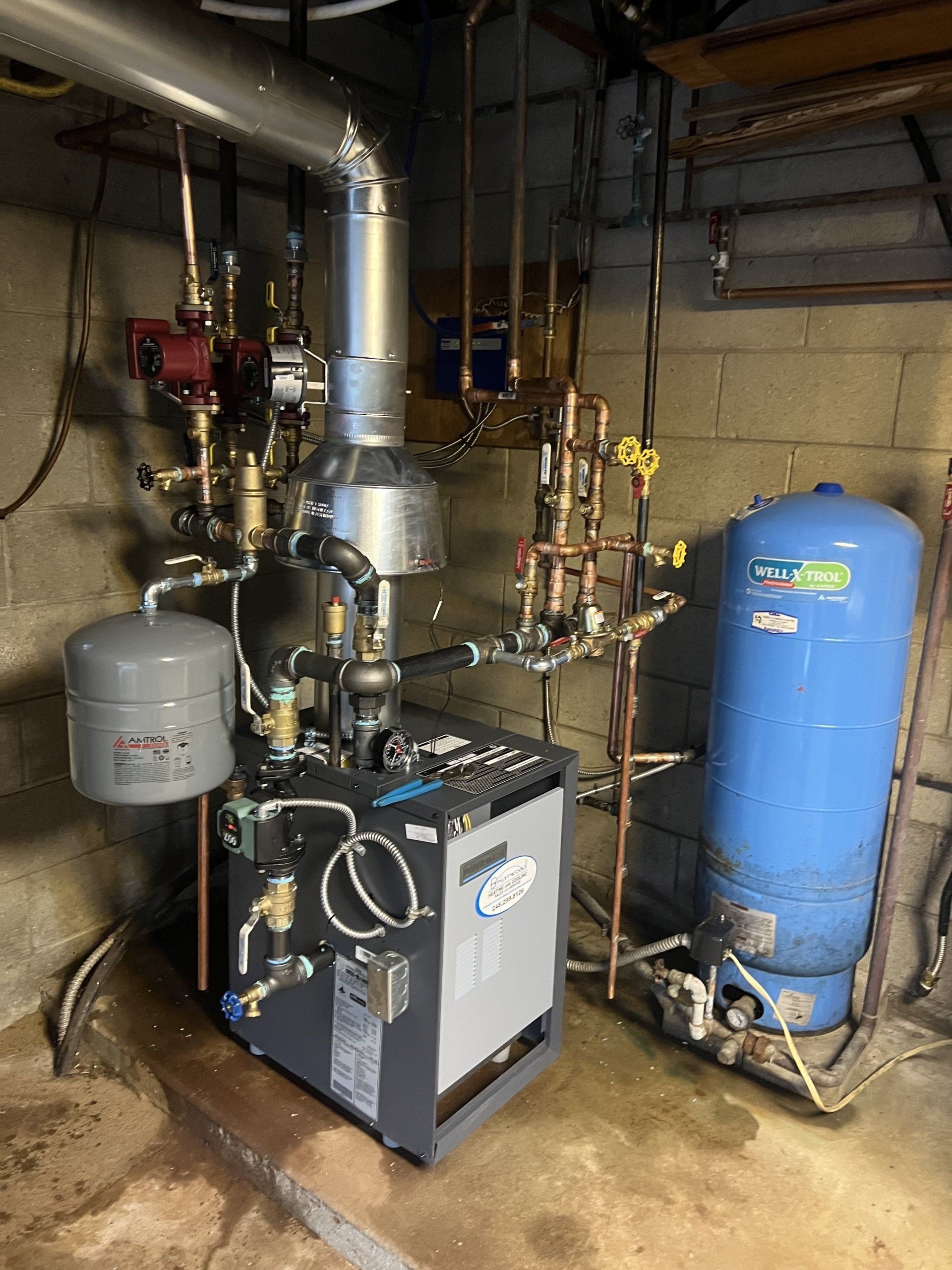 A boiler is sitting in a basement next to a water tank.