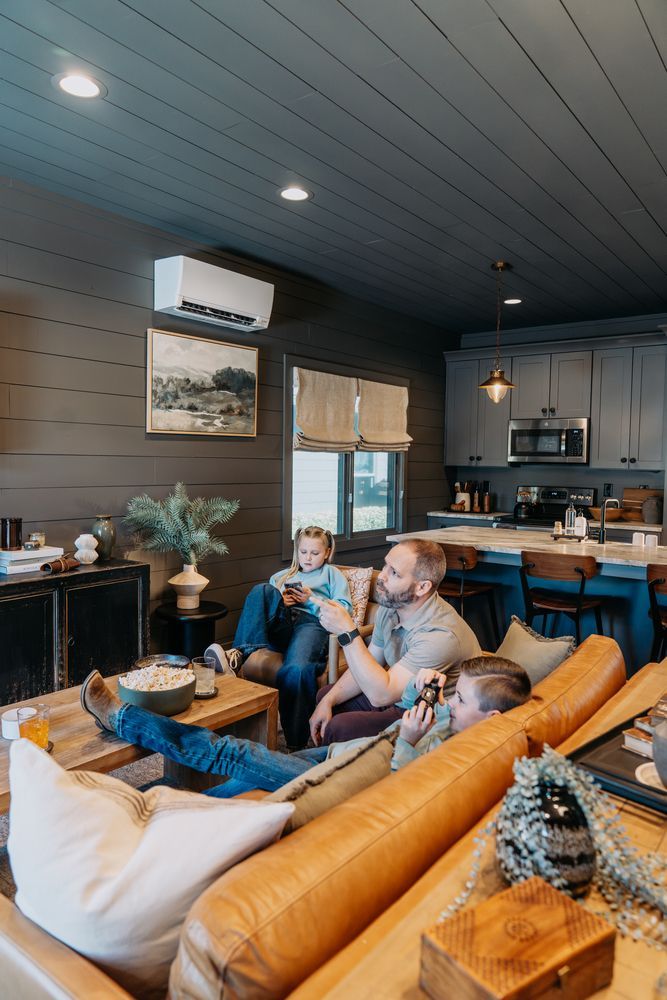 Cozy living room with two people on a tan sectional, fireplace, dark walls, and open kitchen in back