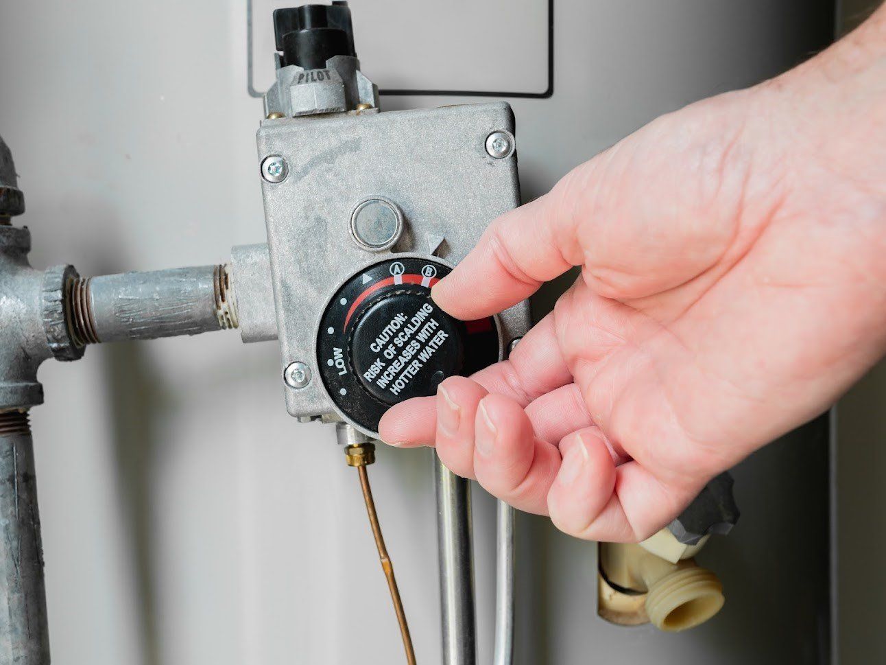 Hand adjusting a boiler thermostat dial on a gray metal heating unit with pipes.