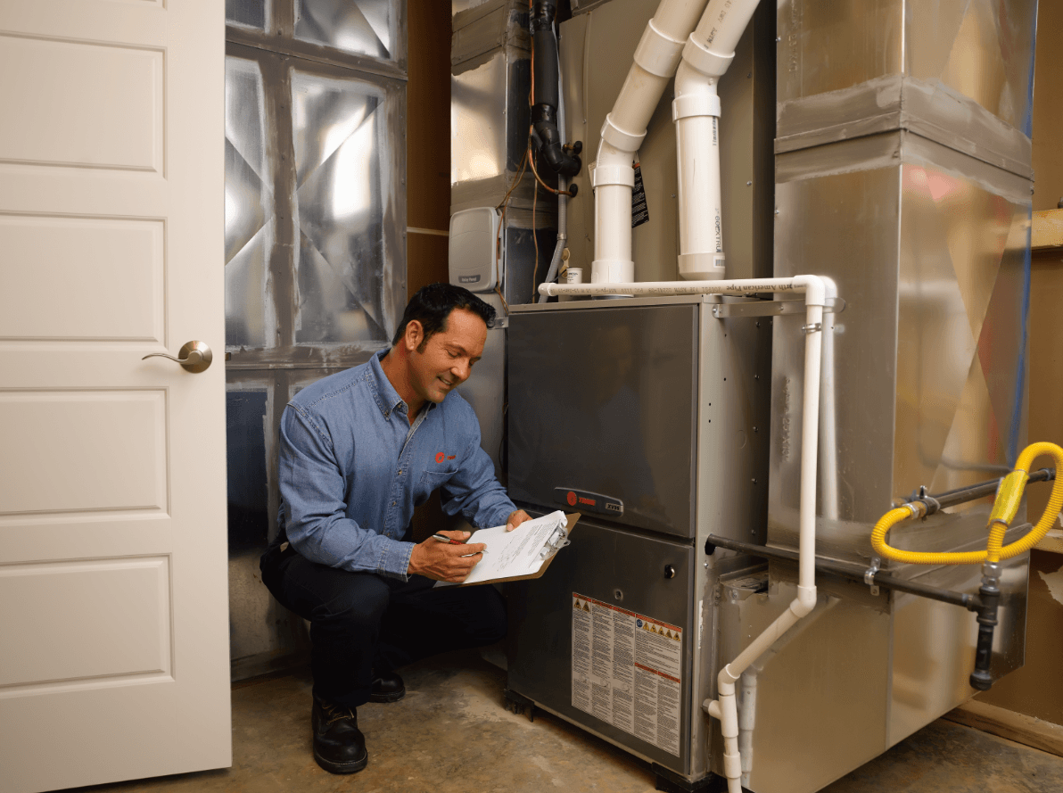 Technician inspecting a furnace unit in a basement, writing on a clipboard.