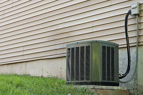 Small Outdoor HVAC — Rochester Hills, MI — Briarwood Heating & Cooling Outdoor central air conditioning unit beside a house wall with beige siding and black hoses