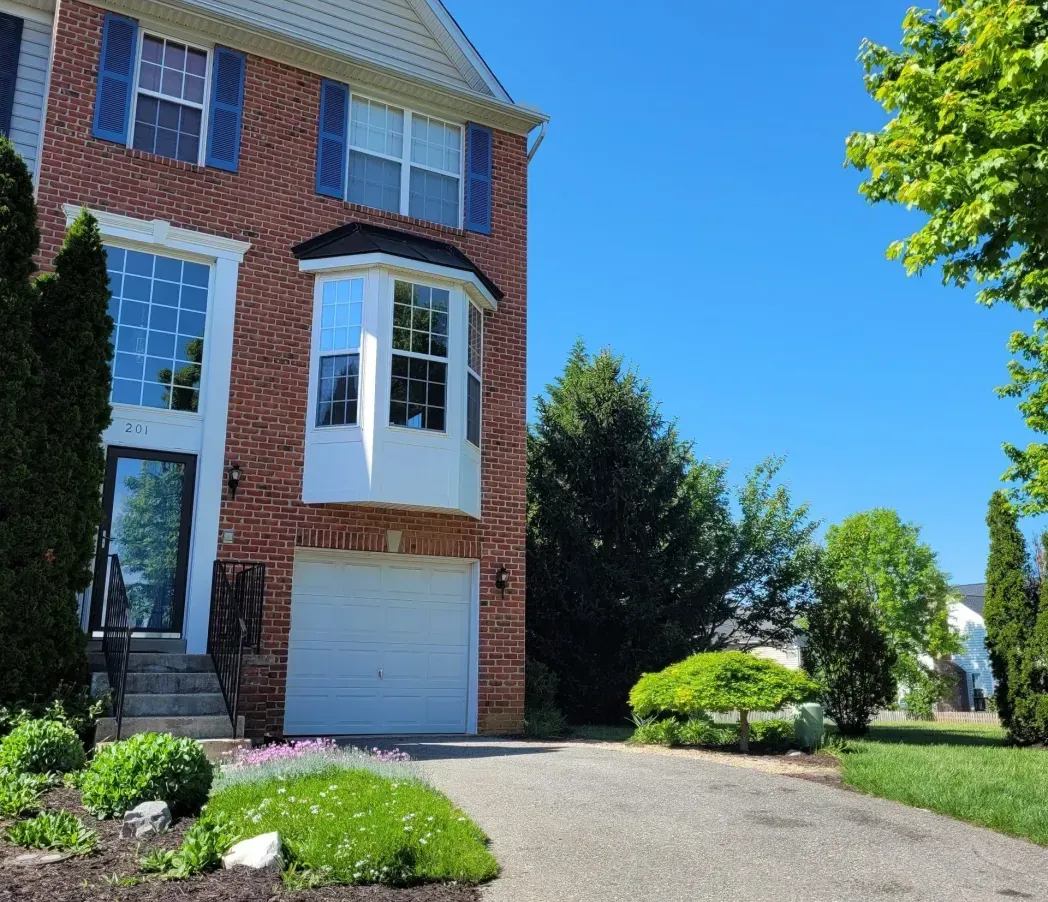 Brick suburban house with white trim, garage, and landscaped front yard under a clear blue sky