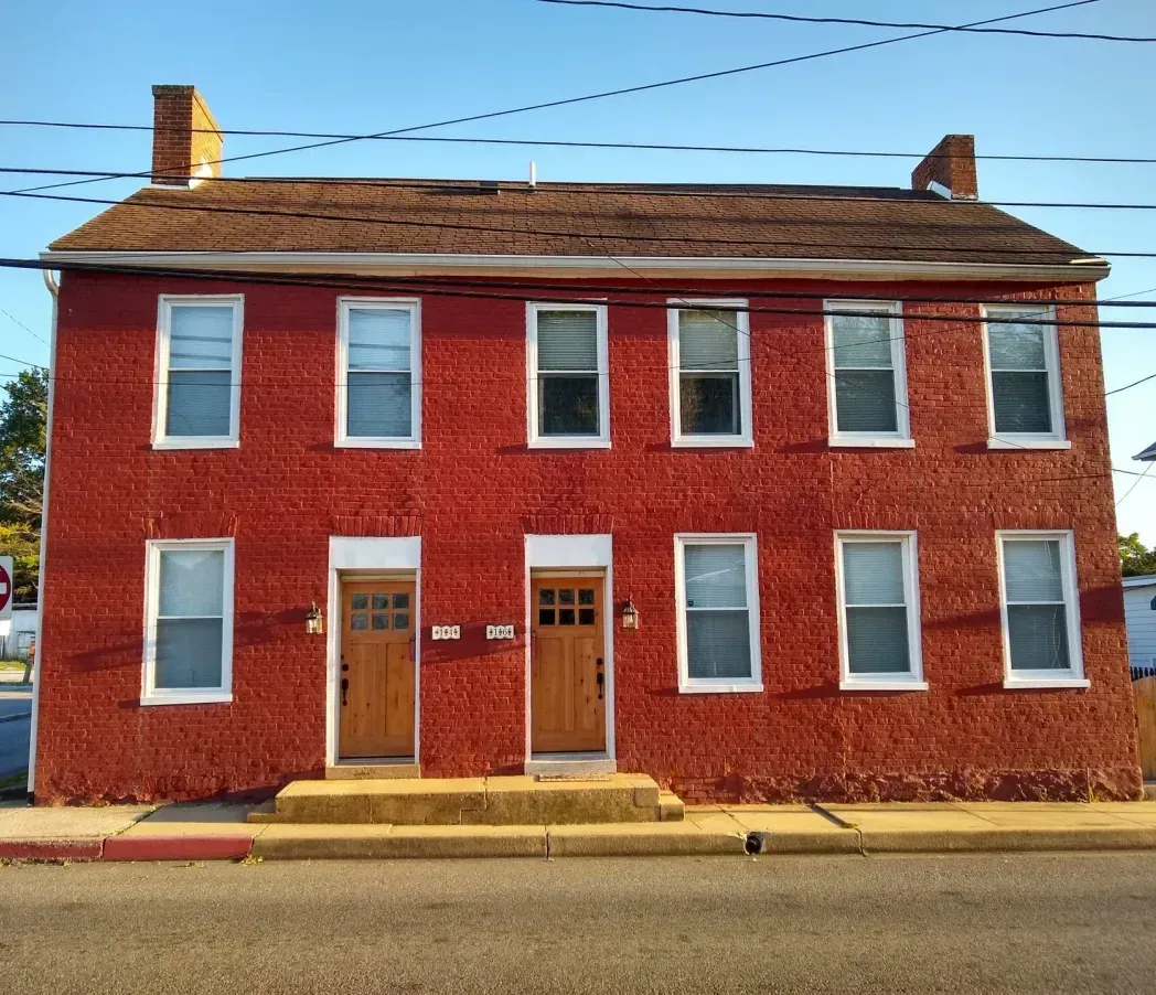 Red brick two-story building with white-trimmed windows and a central doorway on a street corner.