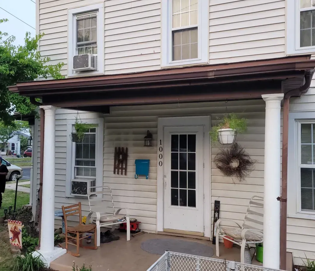 Front porch of a white two-story house with brown roof trim and hanging decor