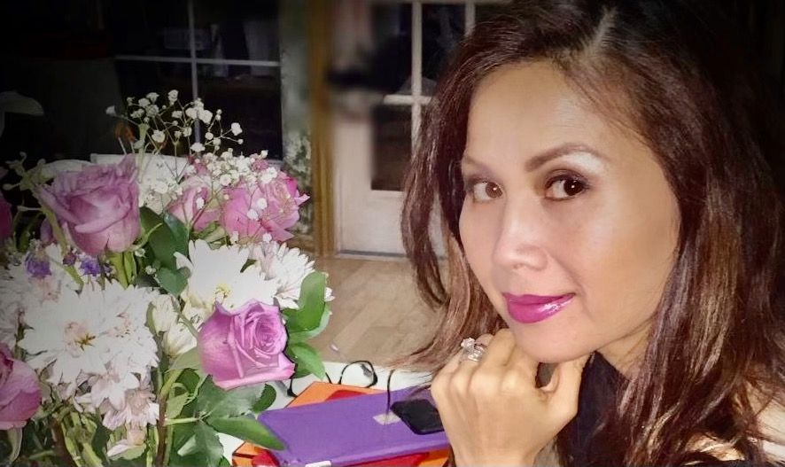 A woman is sitting at a table with flowers in the background.