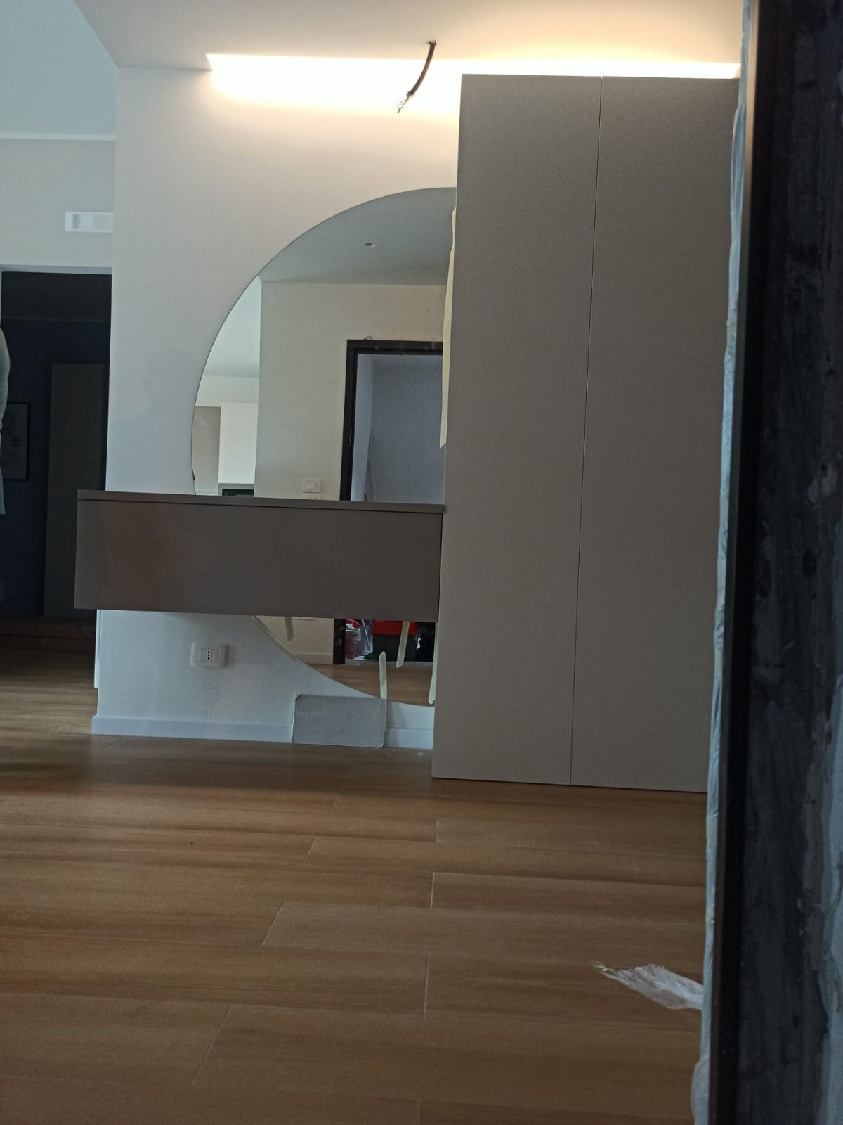 Vista interna: una stanza con pavimento in legno, un grande specchio e un mobile in costruzione.