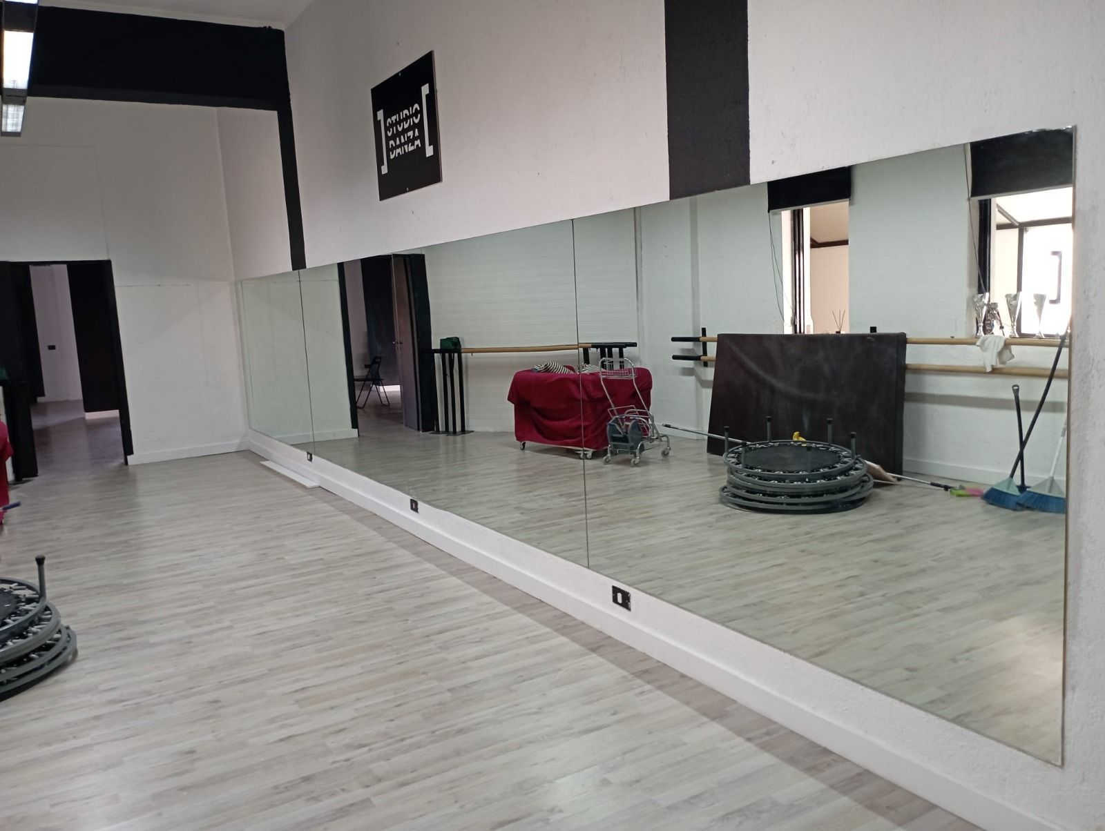 Studio di danza con specchi a tutta altezza, pareti bianche e pavimento in legno chiaro.