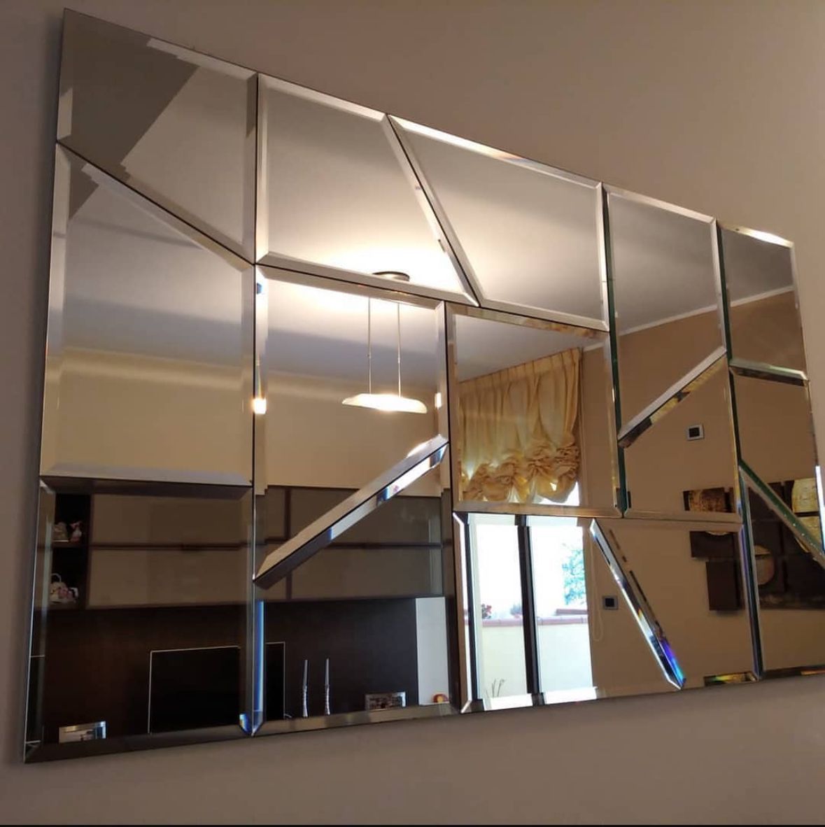 Specchio geometrico sulla parete, che riflette l'interno con finestra, luci e mobili.