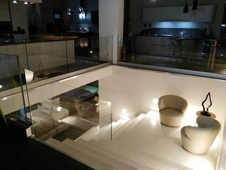 Interni di una casa moderna con scala bianca, ringhiere in vetro e zona salotto.