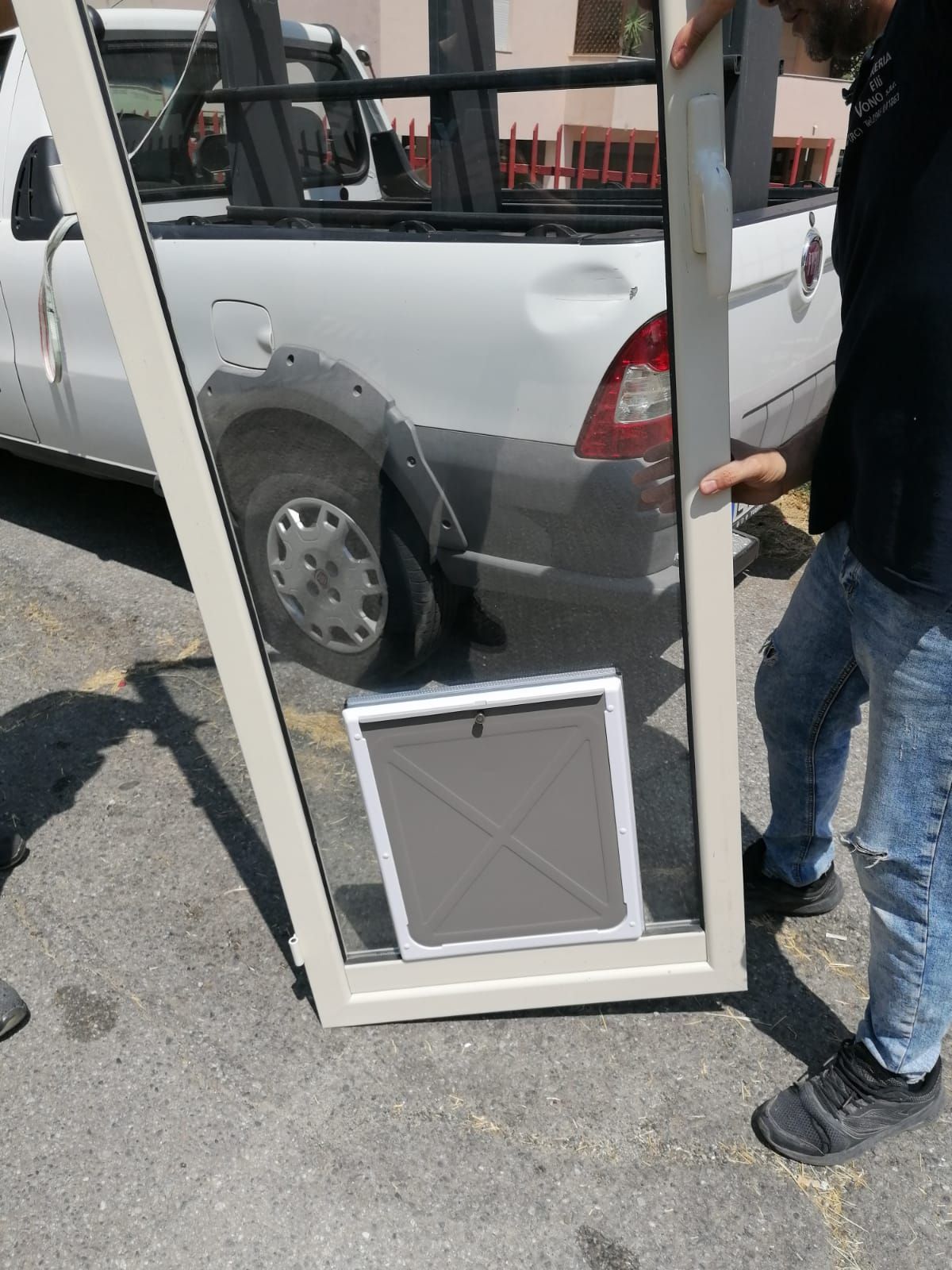 Uomo che tiene aperta una finestra con una porticina per animali domestici, accanto a un camion bianco.