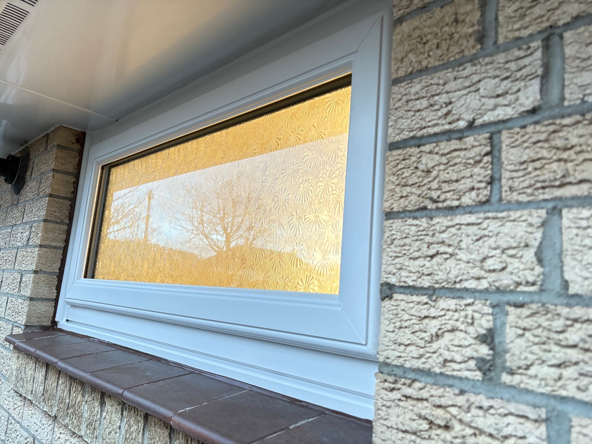 White-framed window on a brick building, reflecting a golden-hued tree, with a brown windowsill.
