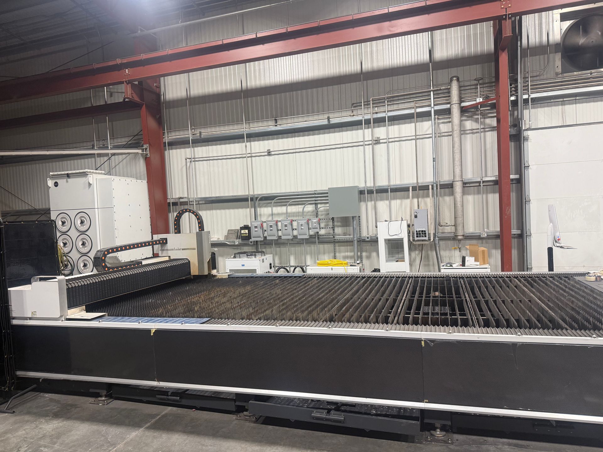 Large industrial CNC cutting machine in a workshop, with metal rails and red steel beams in the background