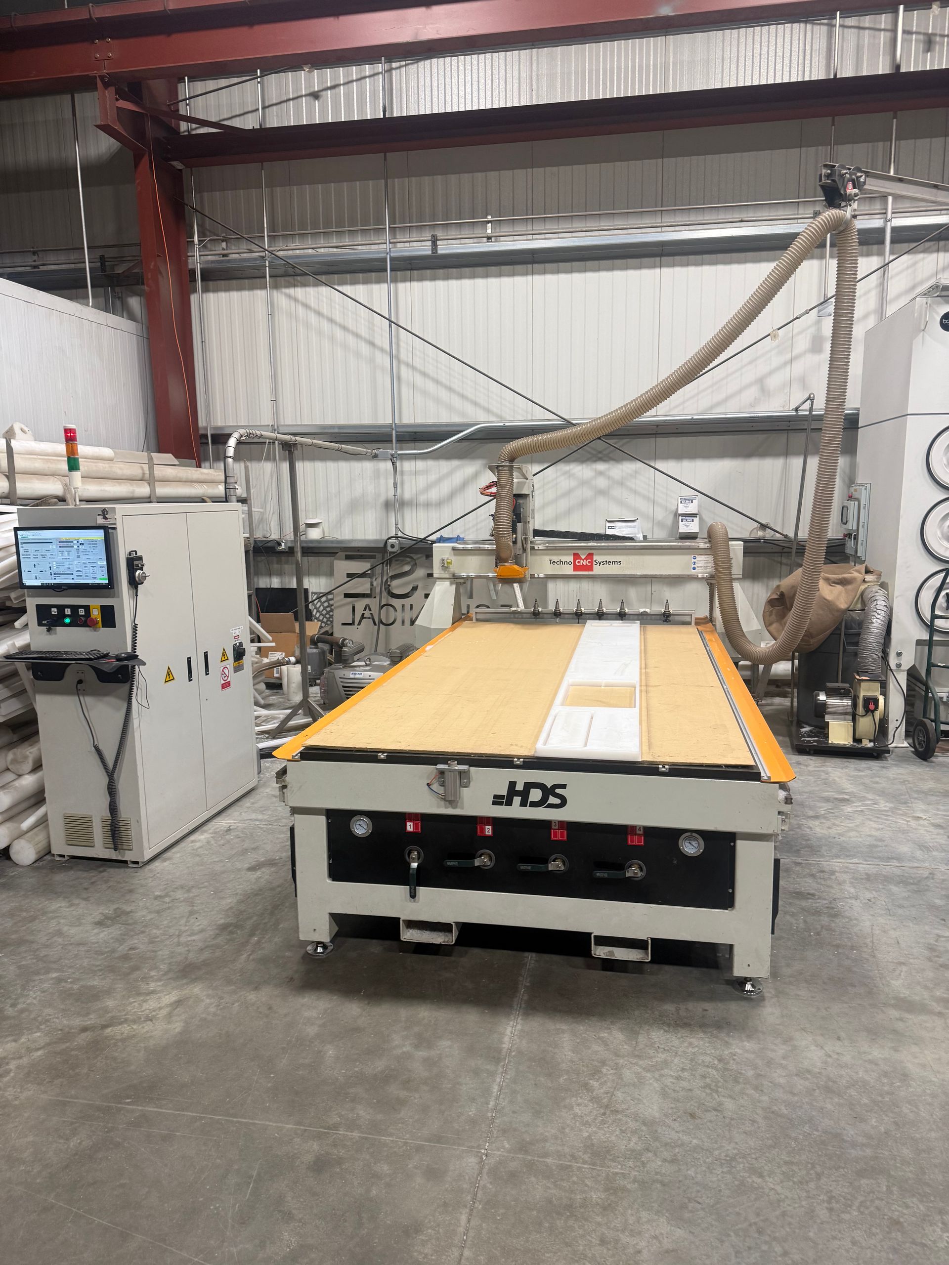 Industrial shop with a large CNC cutting table, control panel, and overhead gantry in a warehouse.