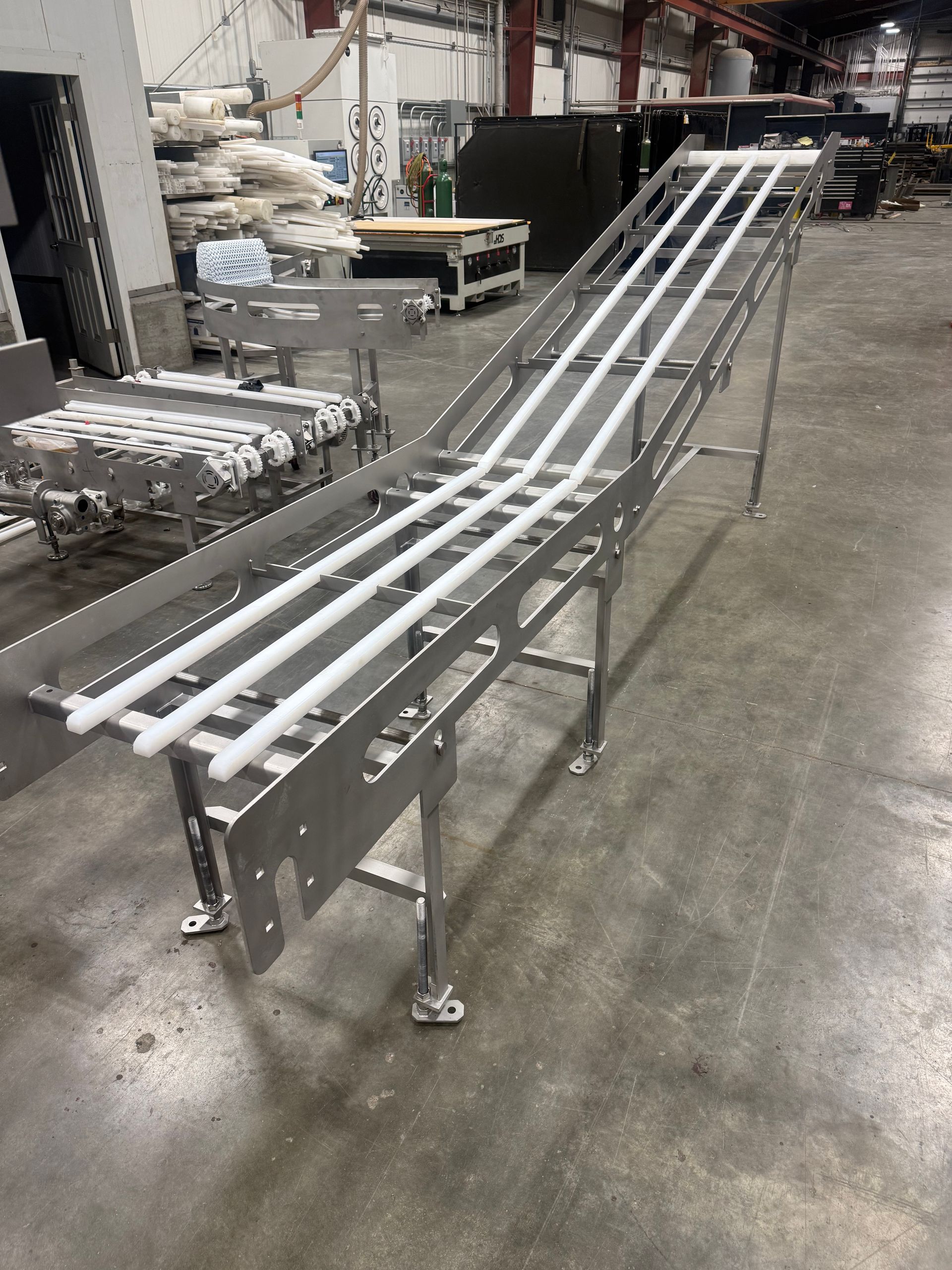 Long metal conveyor frame with white rails in an industrial workshop.