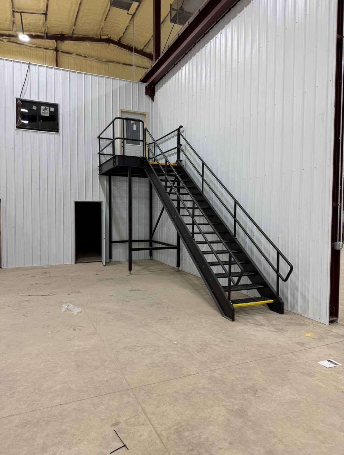 Industrial warehouse interior with metal staircase leading to a small landing and door.