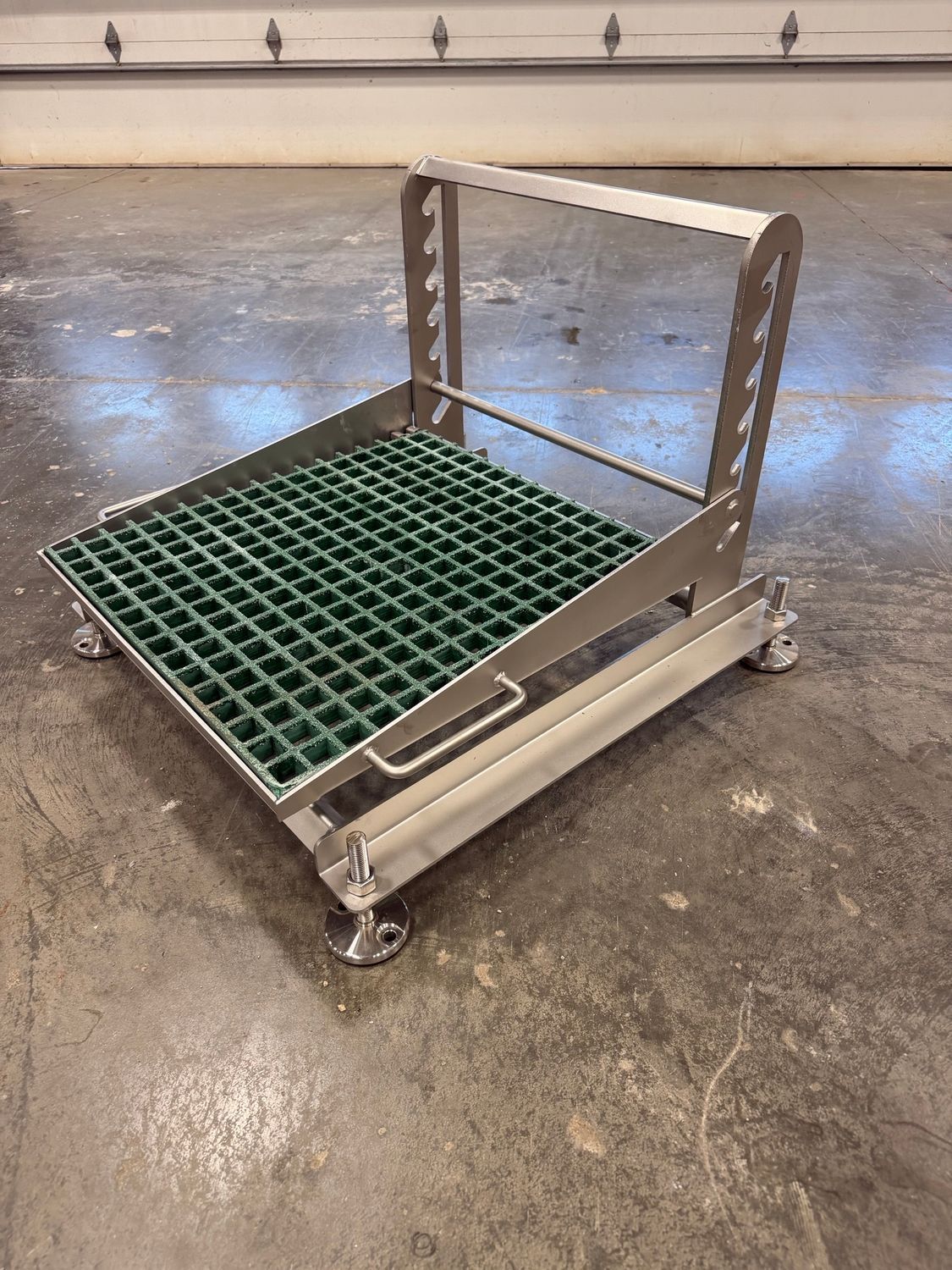Metal rolling cart with a green grated platform in a warehouse or workshop floor