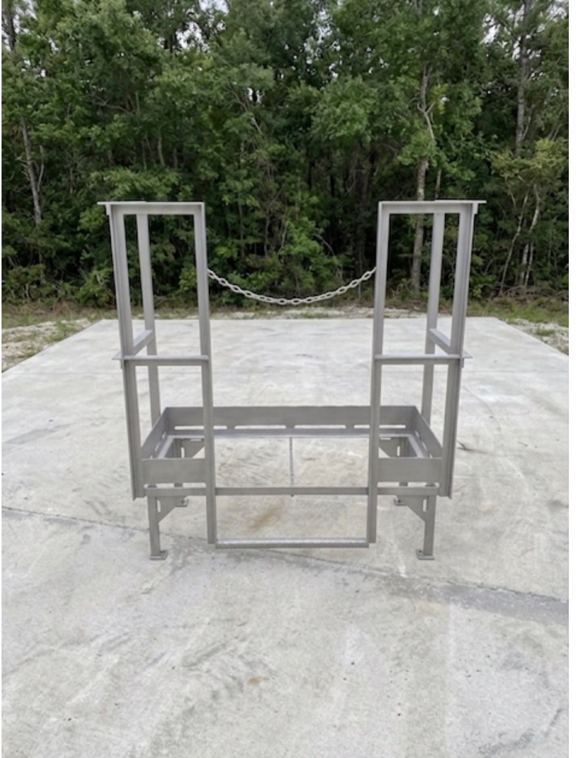 Metal frame cart or rack on concrete, with trees in the background.