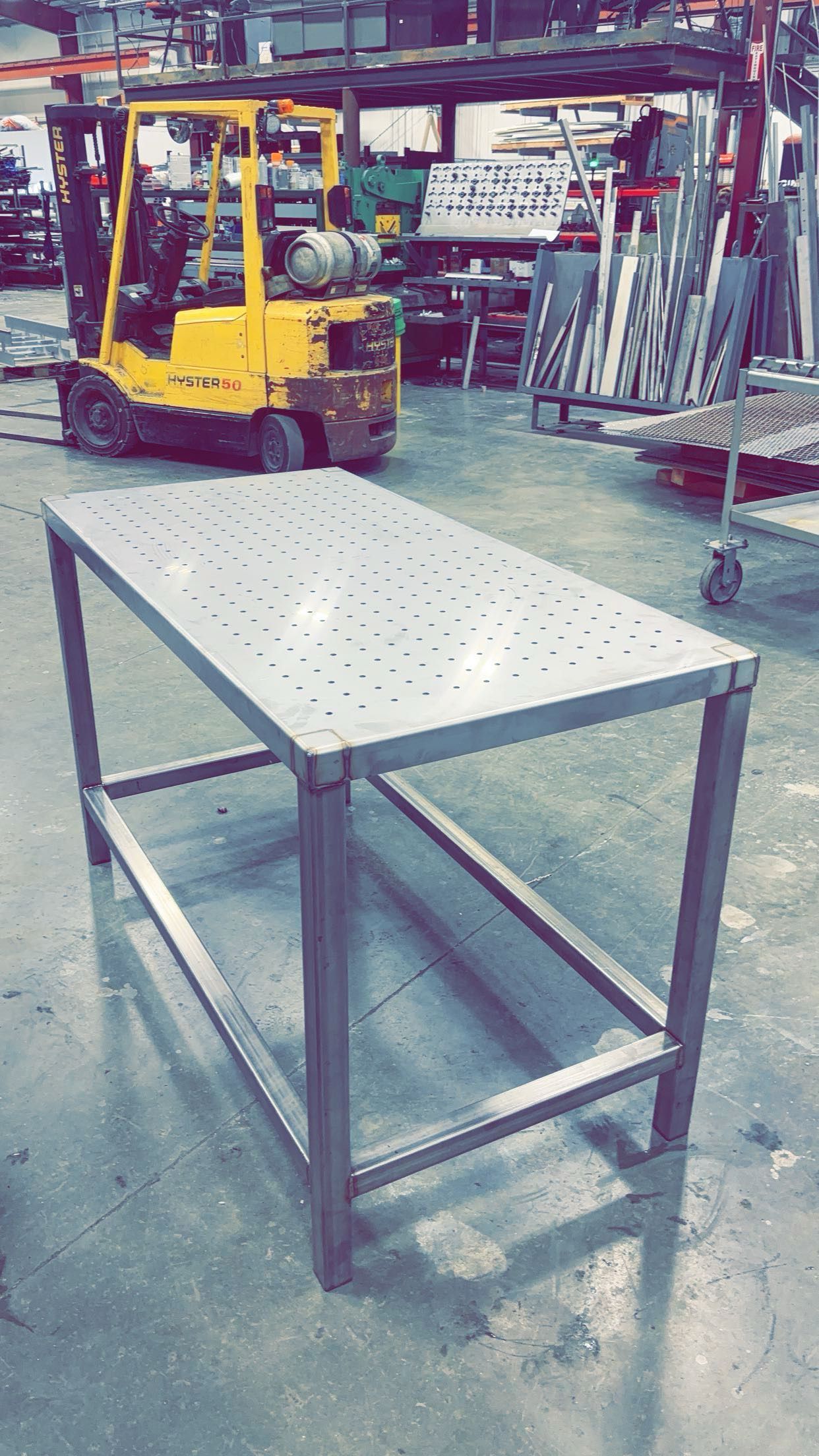 Yellow forklift in an industrial warehouse behind a metal worktable with a white perforated top