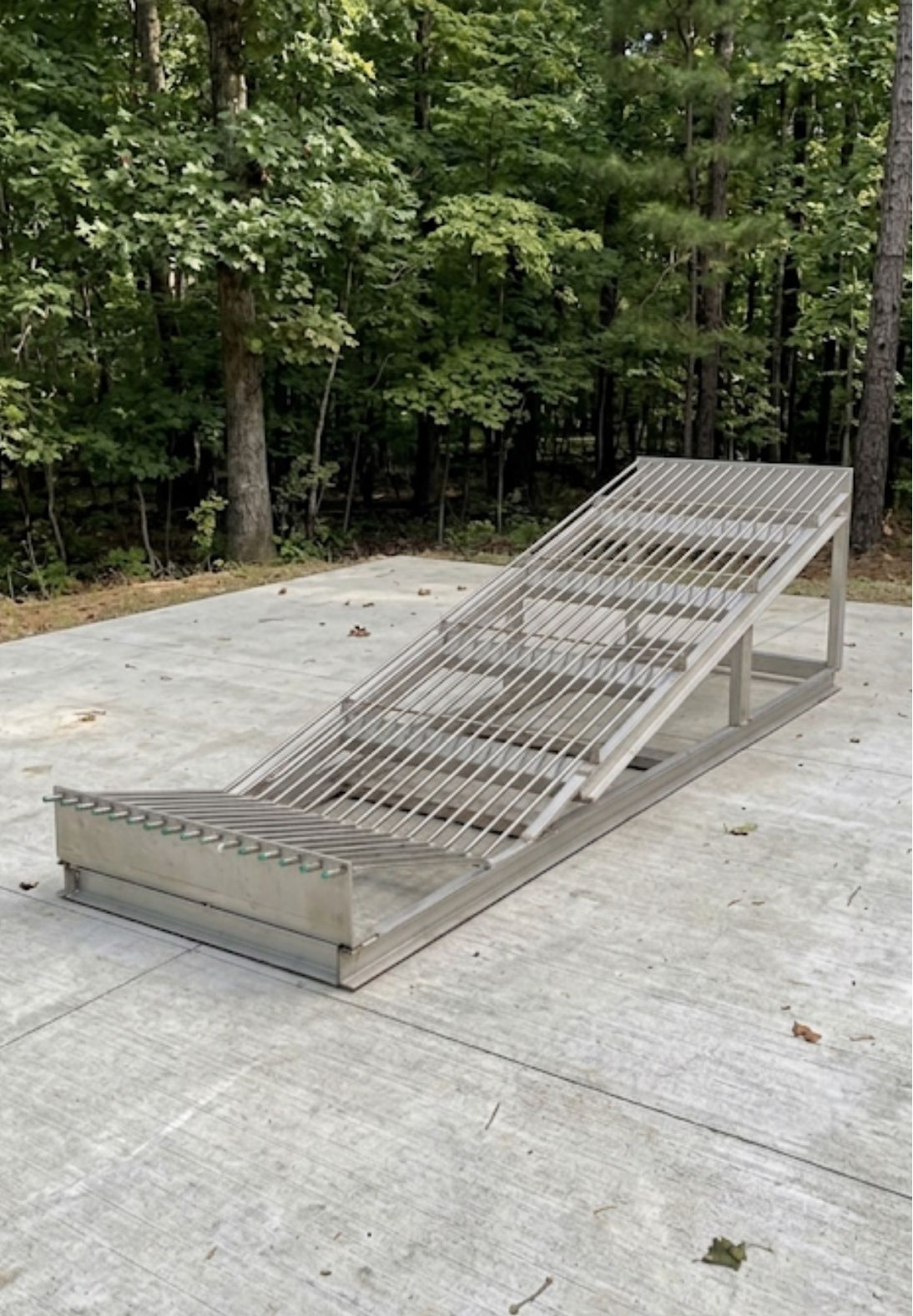 Metal skate ramp on a concrete pad beside a wooded area