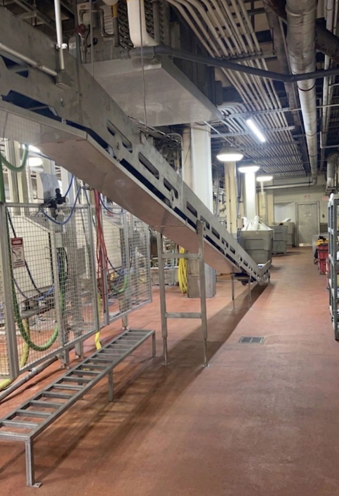 Industrial conveyor line in a factory, with metal machinery overhead and a red walkway below.