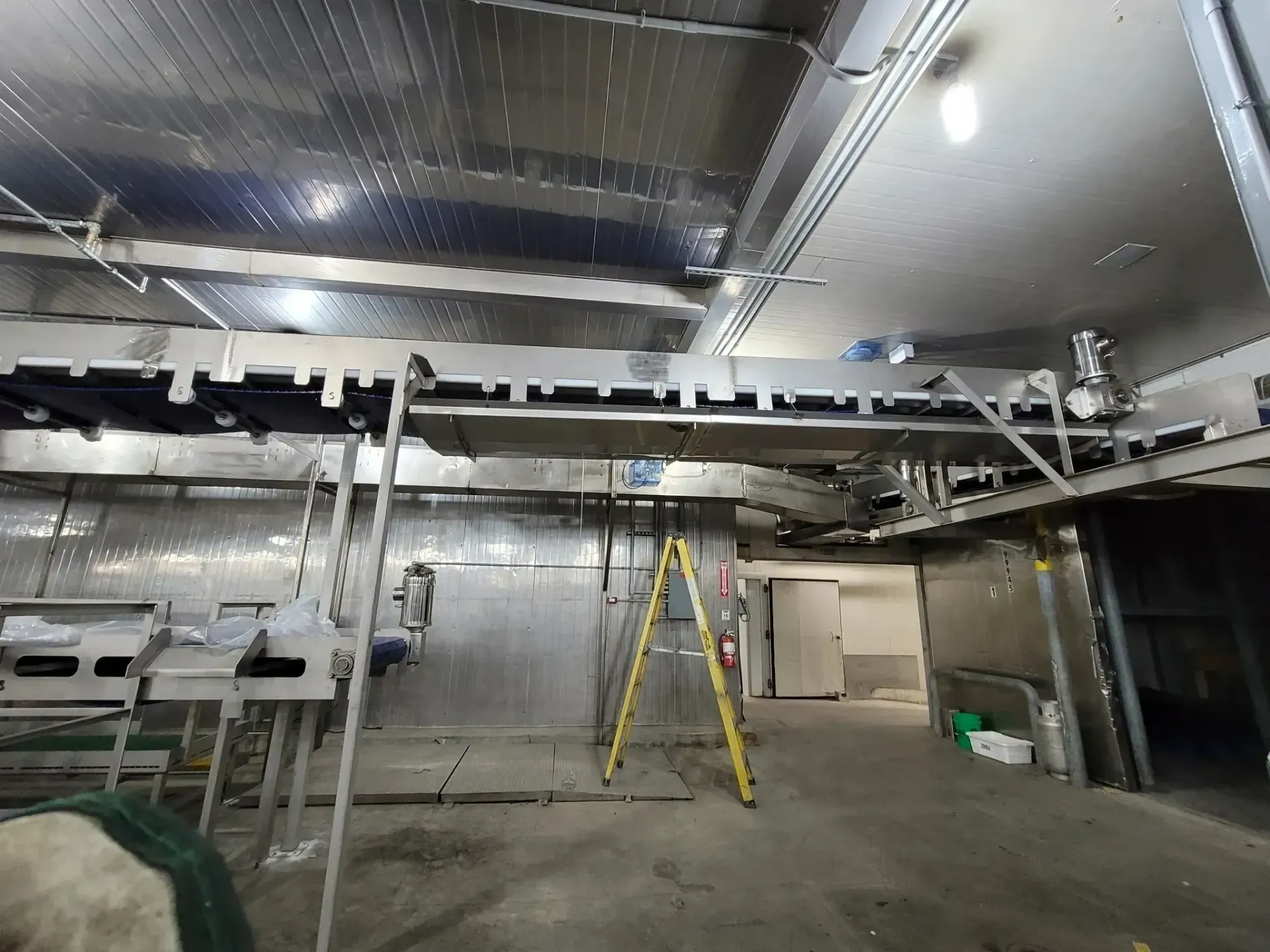 Industrial utility room with metal ducting, pipes, and a yellow ladder under bright ceiling lights.