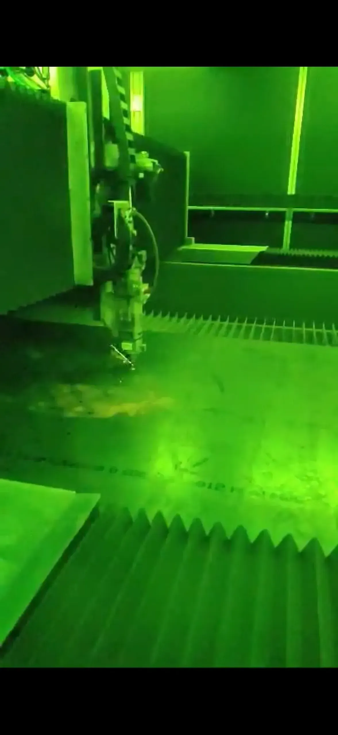 Green-tinted industrial machine inspecting a corrugated metal surface in a factory setting