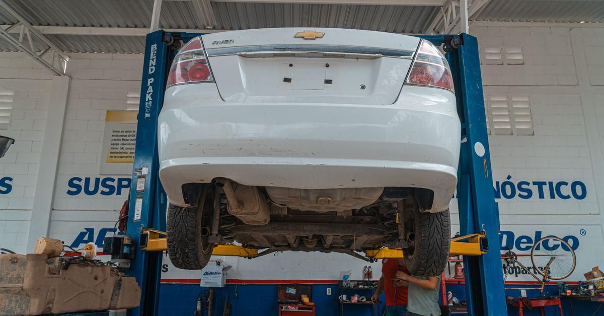 Coche blanco elevado en una plataforma elevadora azul de un taller mecánico, con los bajos al descubierto