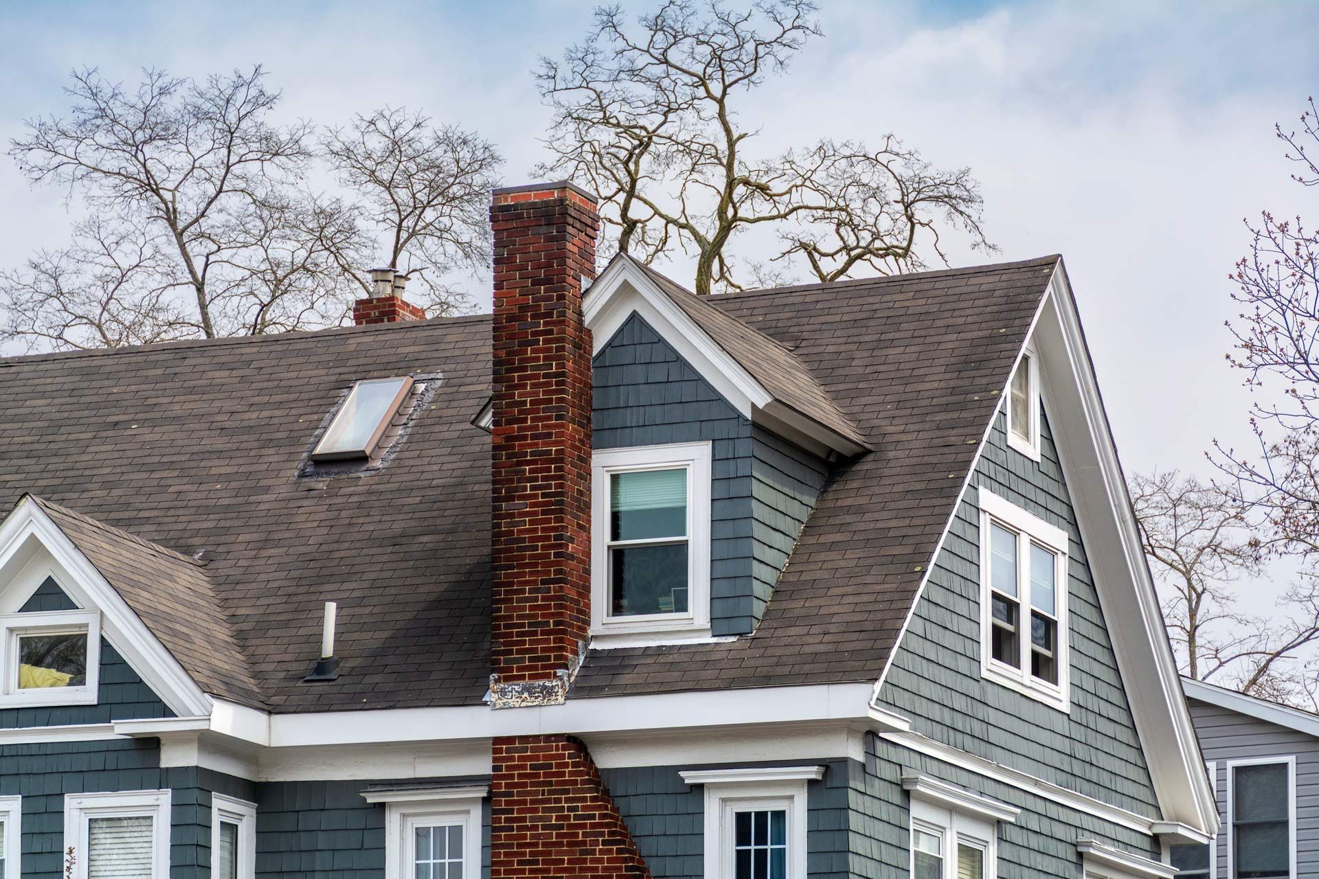 Gray house with white trim and red brick chimney under leafless trees, seen from below