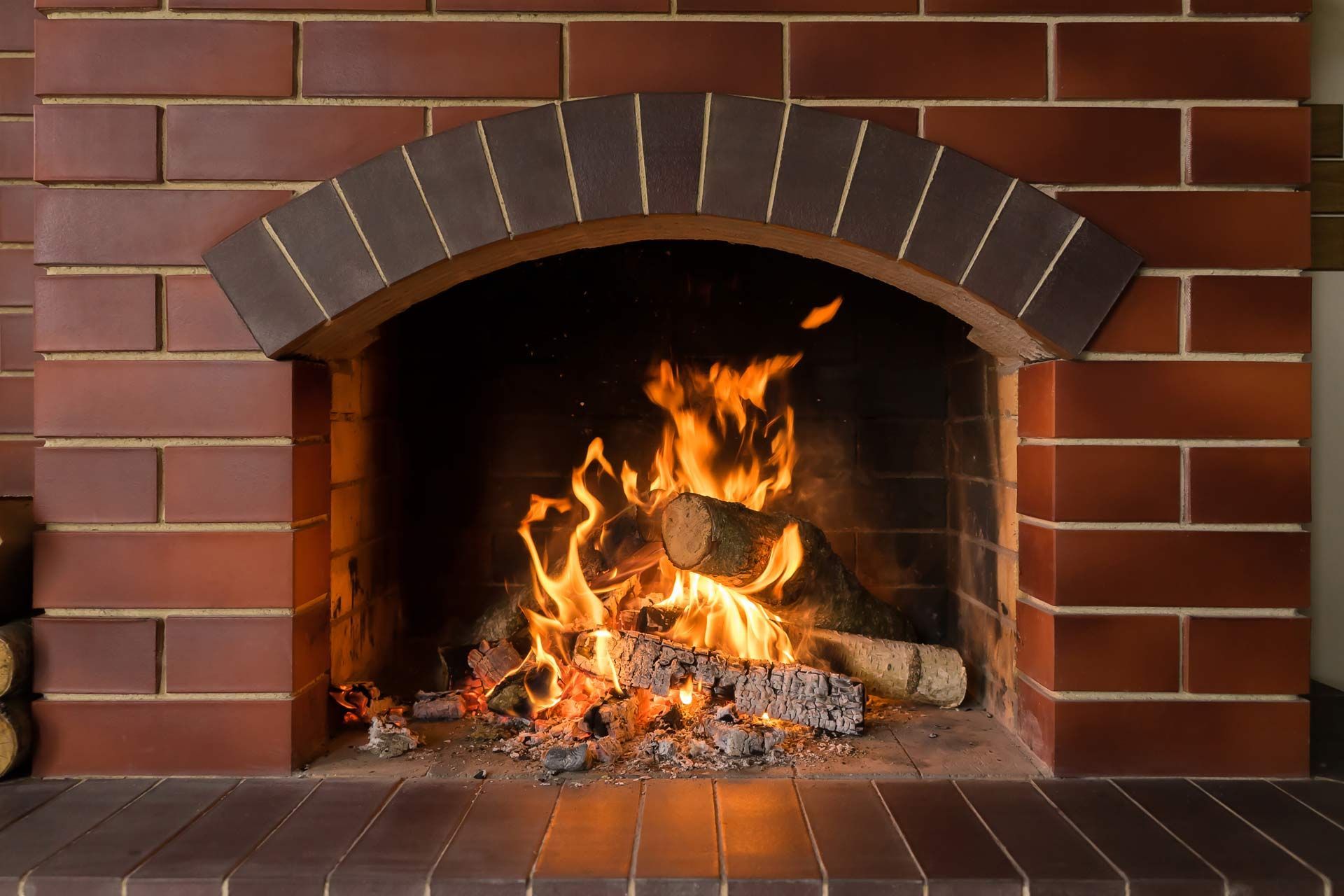Brick fireplace with a burning fire and glowing logs inside.