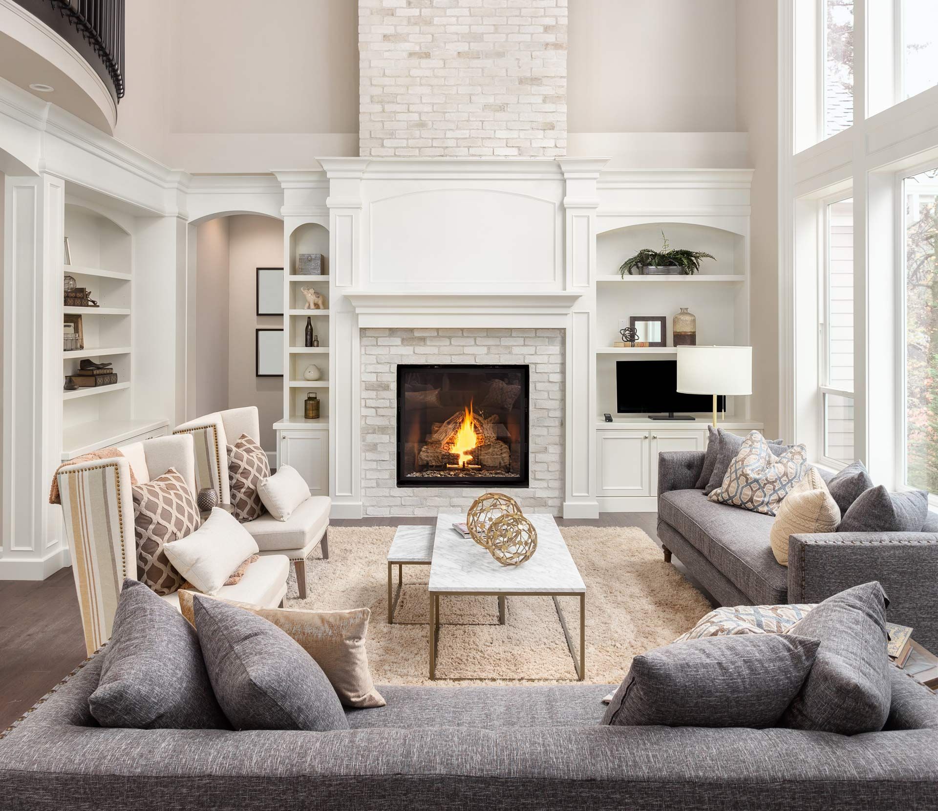 Bright, airy living room with gray sofas, white fireplace, and tall windows