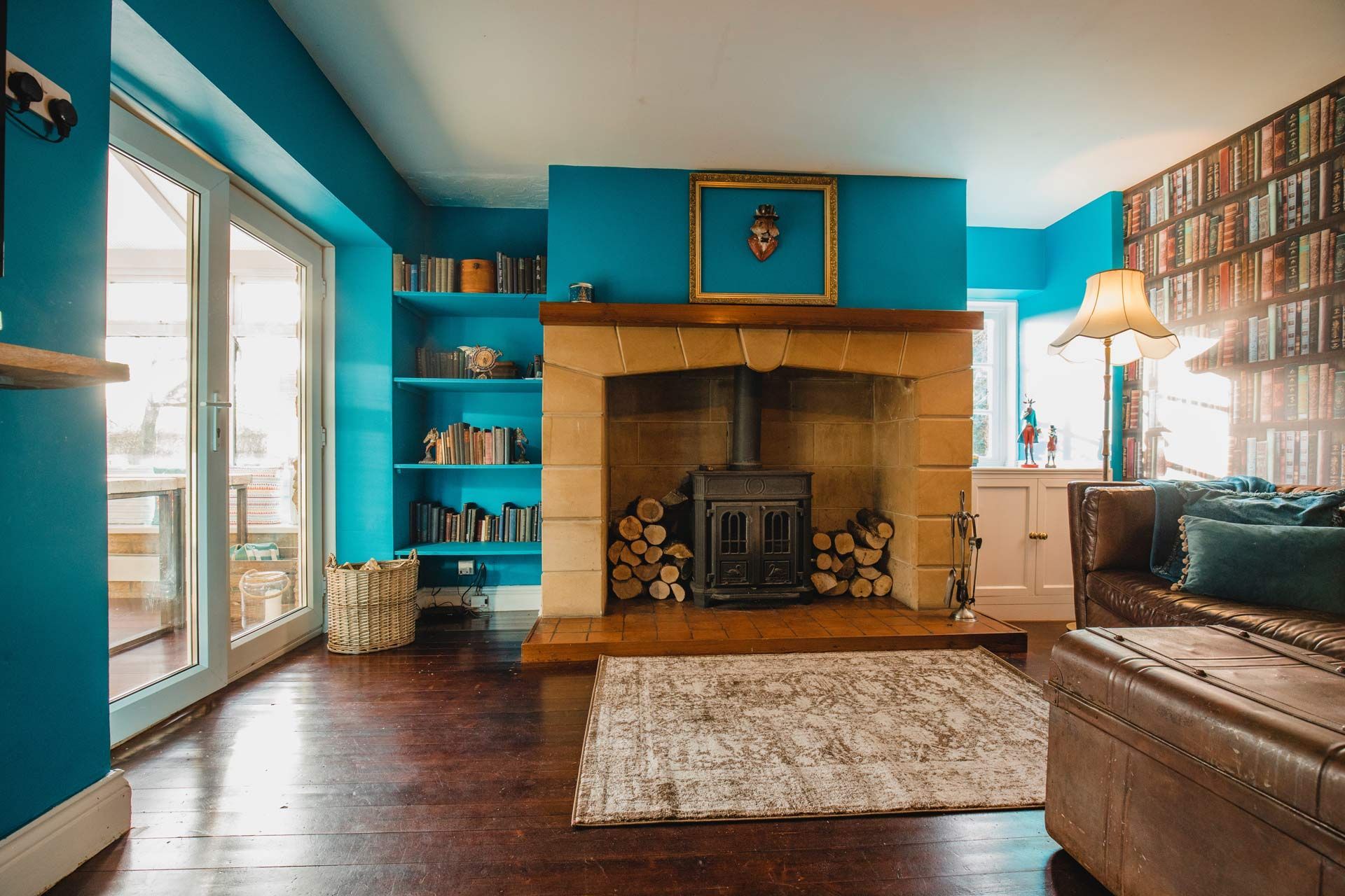 Bright living room with turquoise walls, wood fireplace, sofa, shelves, and large windows.