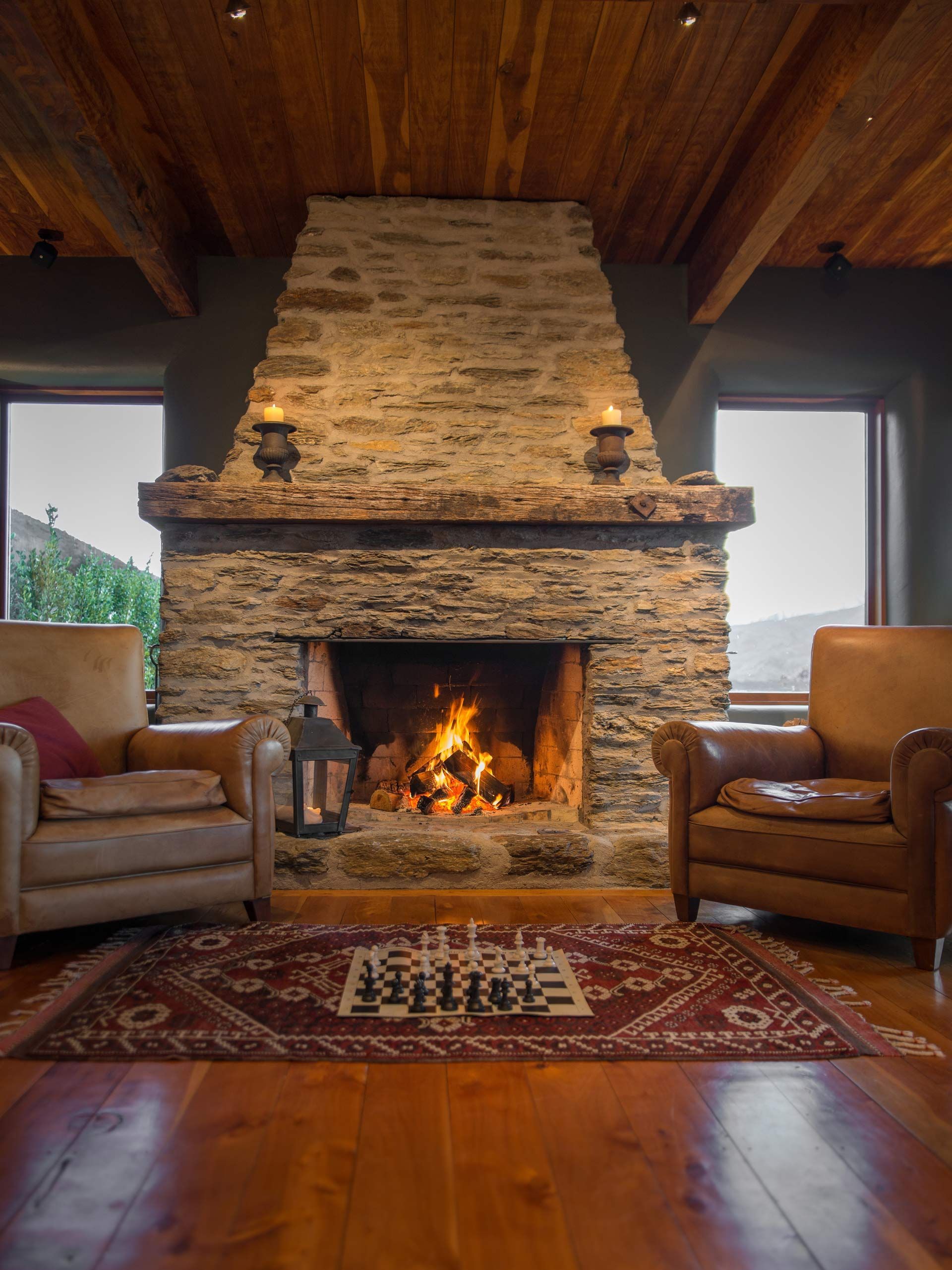 Cozy living room with stone fireplace, two armchairs, wooden ceiling, and patterned rug.