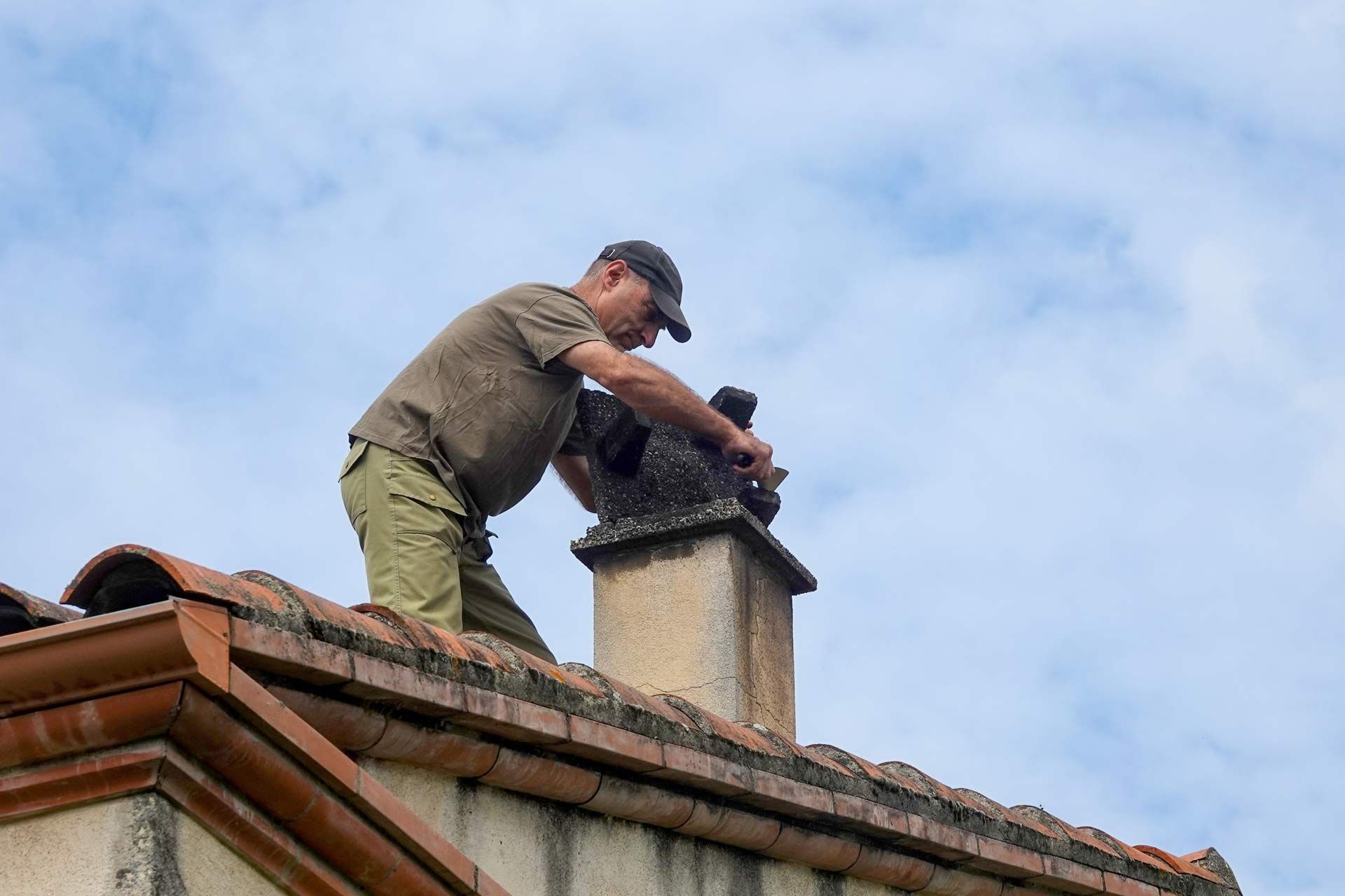 Worker repairing a chimney on a rooftop under a blue sky.