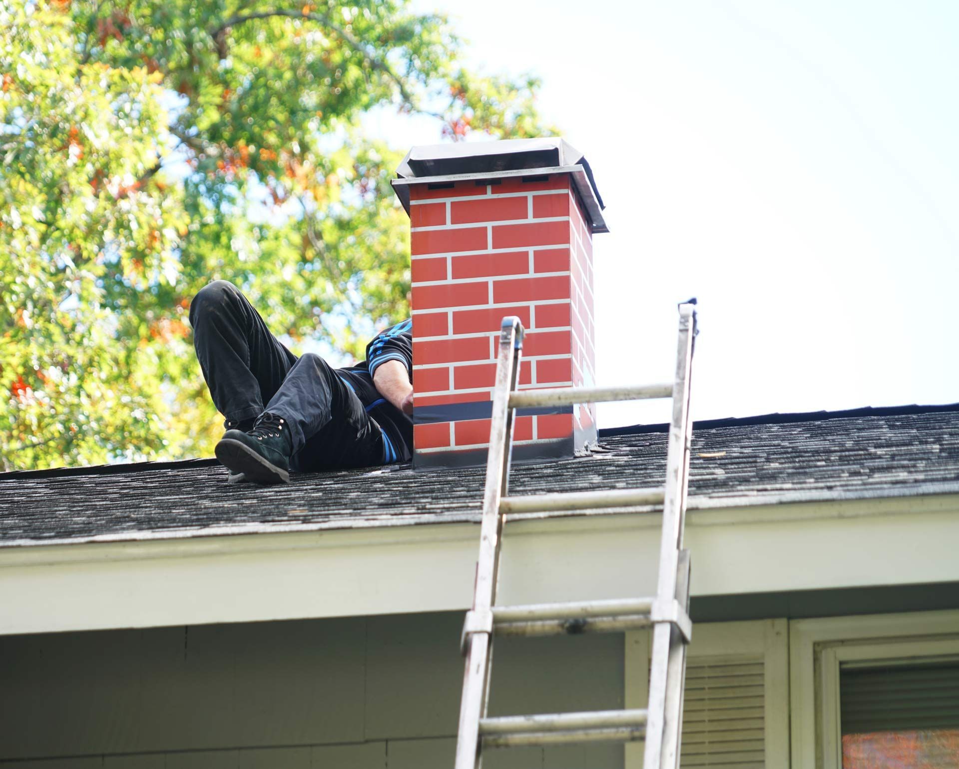 Person lying on a roof beside a chimney, with a ladder leaning up from below.