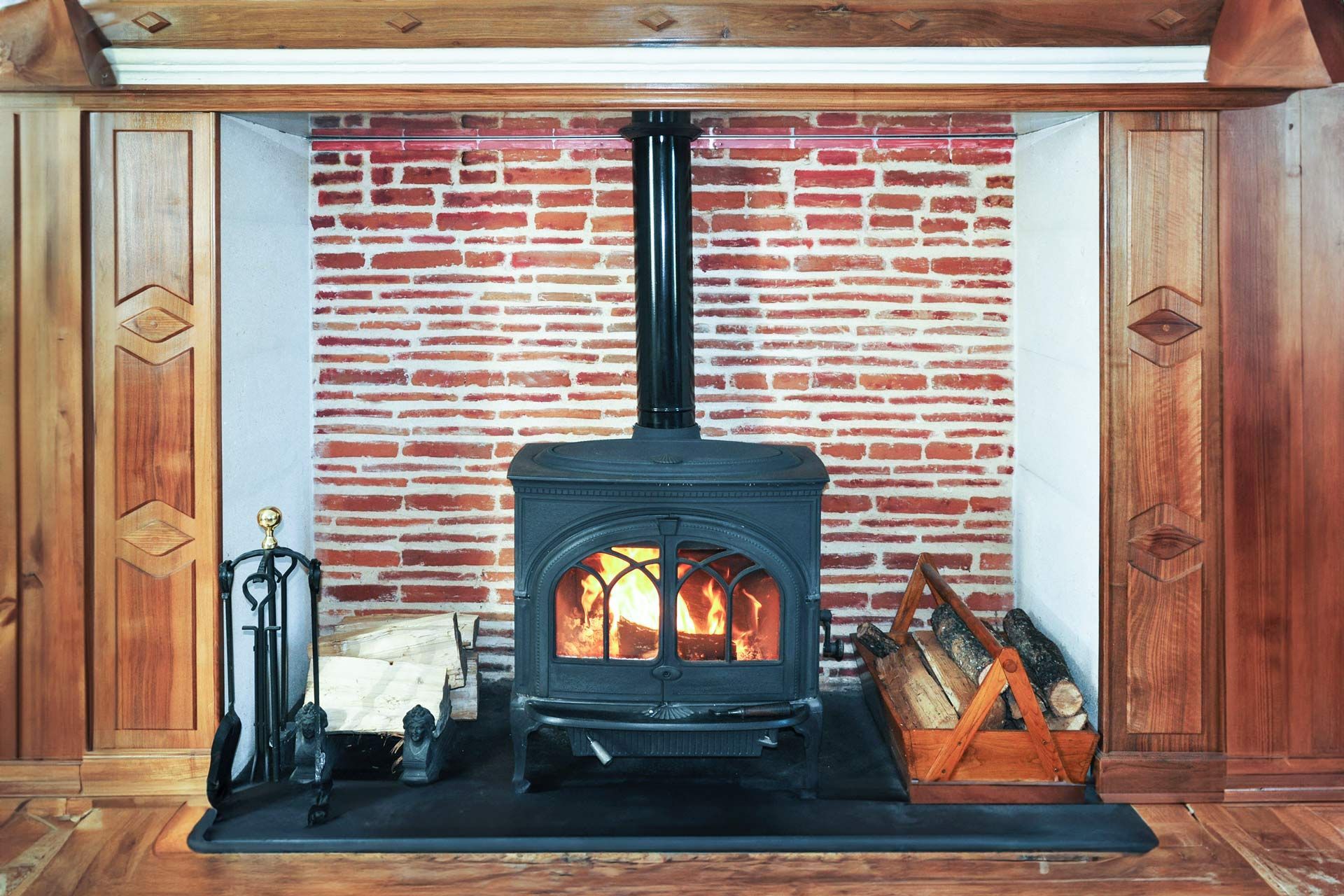 Wood-burning stove in a wooden hearth with brick backing and fire tools on either side