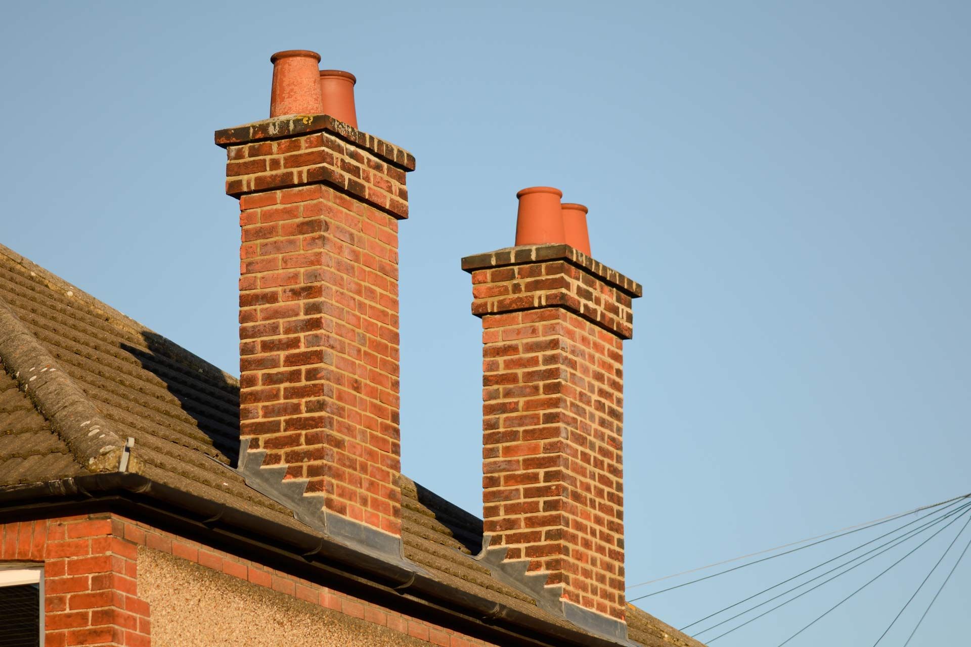 Two brick chimneys on a tiled roof against a blue sky