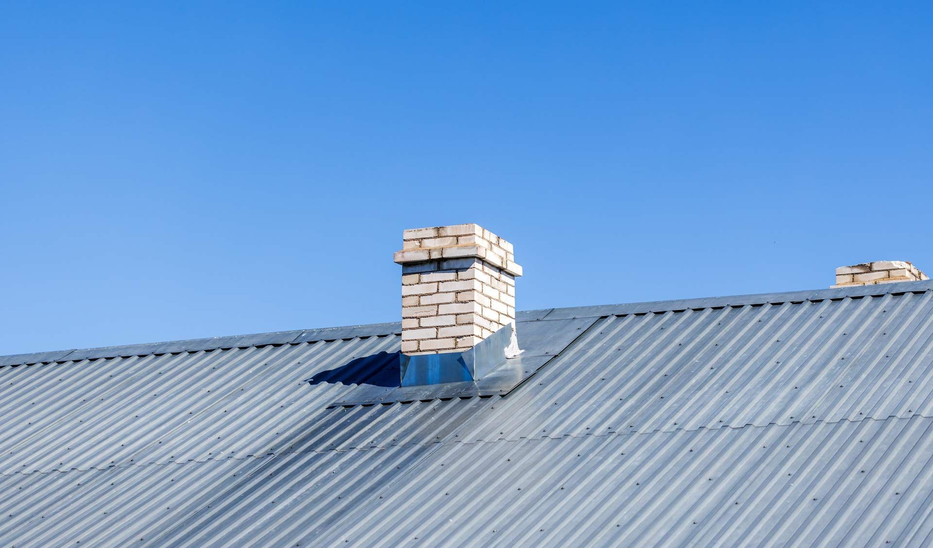 Corrugated metal roof with a brick chimney against a clear blue sky