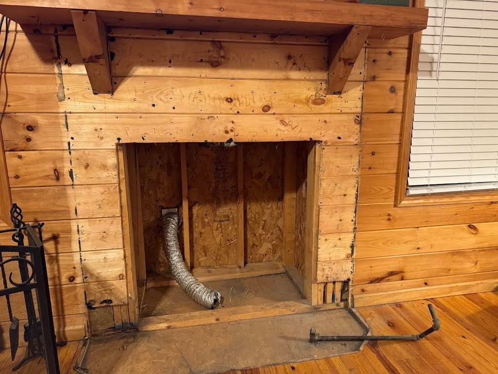 Wood-paneled fireplace opening with exposed ducting in a rustic room