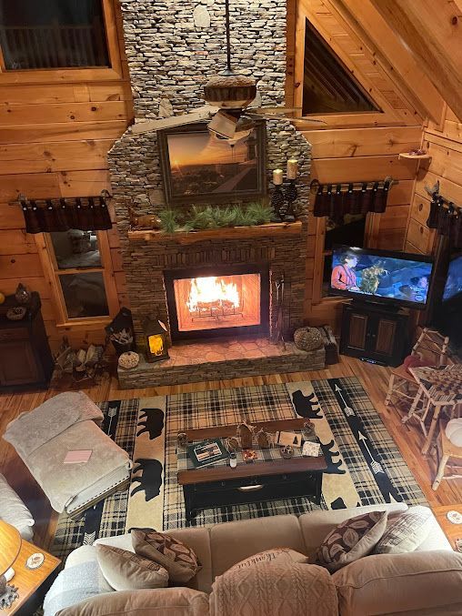 Cozy rustic living room with a stone fireplace, wood walls, and a mounted TV beside a couch and rug.