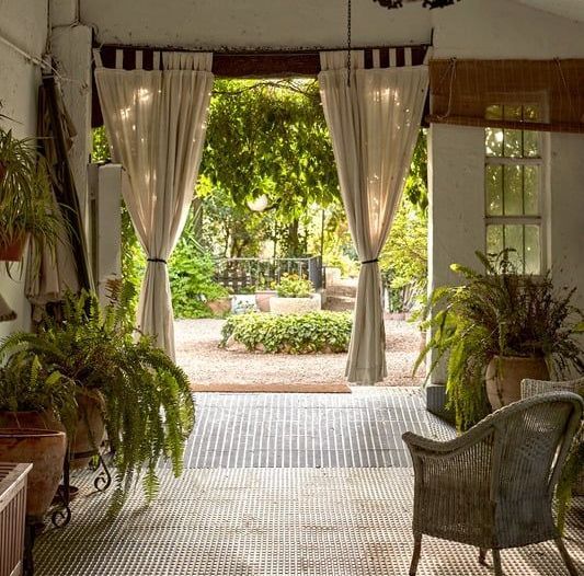 Open-air room with ferns, view of lush garden through draped doorway, beige tones.