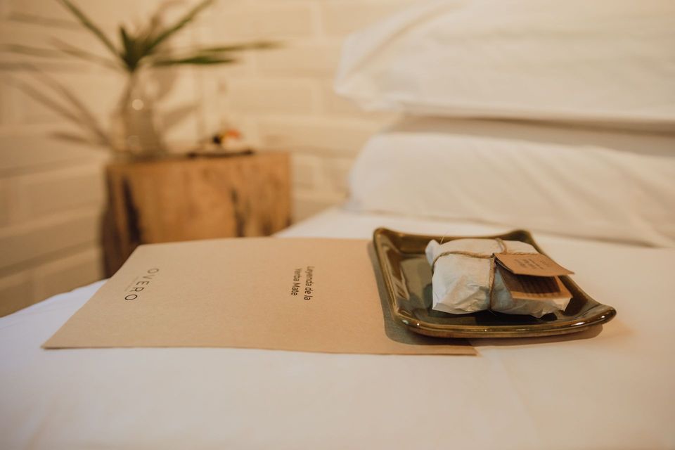 Cama de hotel con mesita de noche y una bandeja de bienvenida, ofreciendo una experiencia auténtica en Overo Iguazú.
