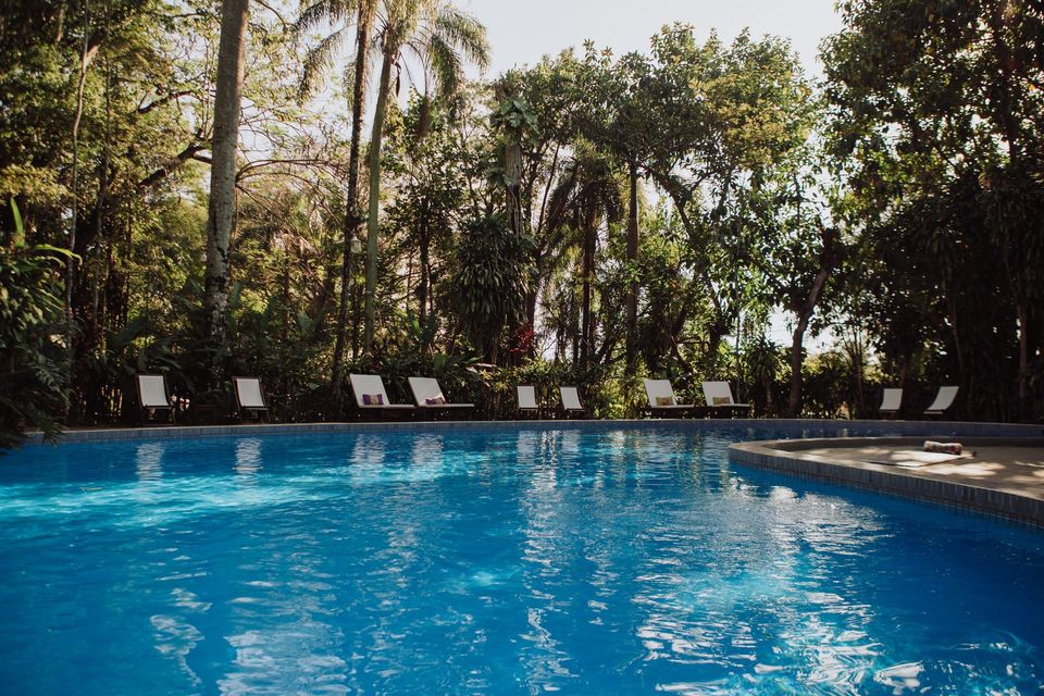 Piscina exterior de Overo Iguazú Lodge rodeada de exuberante vegetación y árboles tropicales.