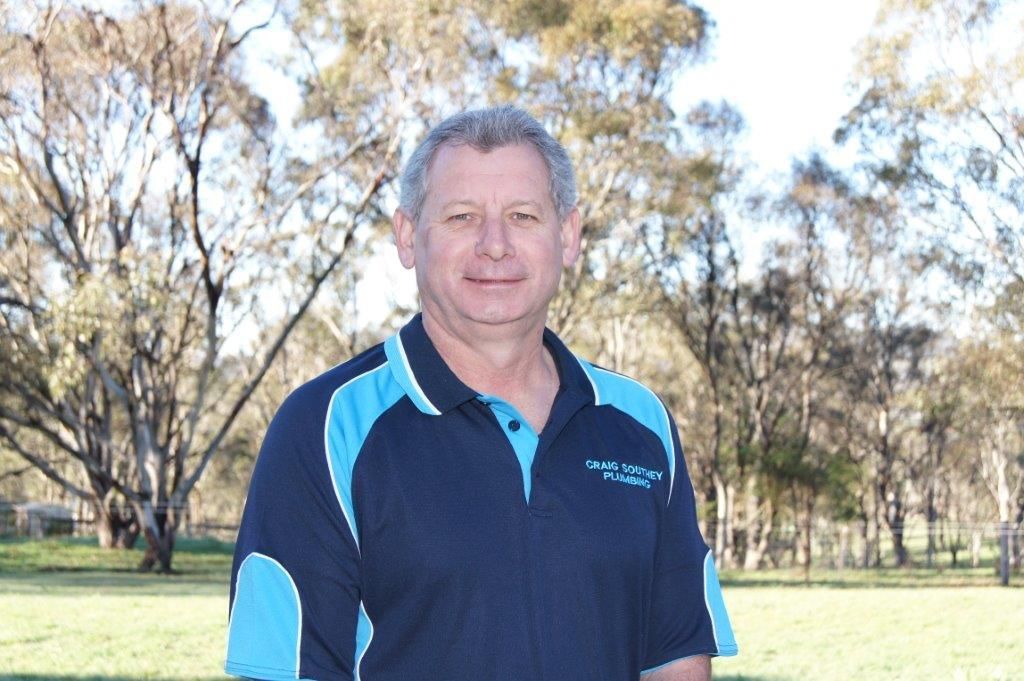 A man in a blue shirt is standing in a field with trees in the background