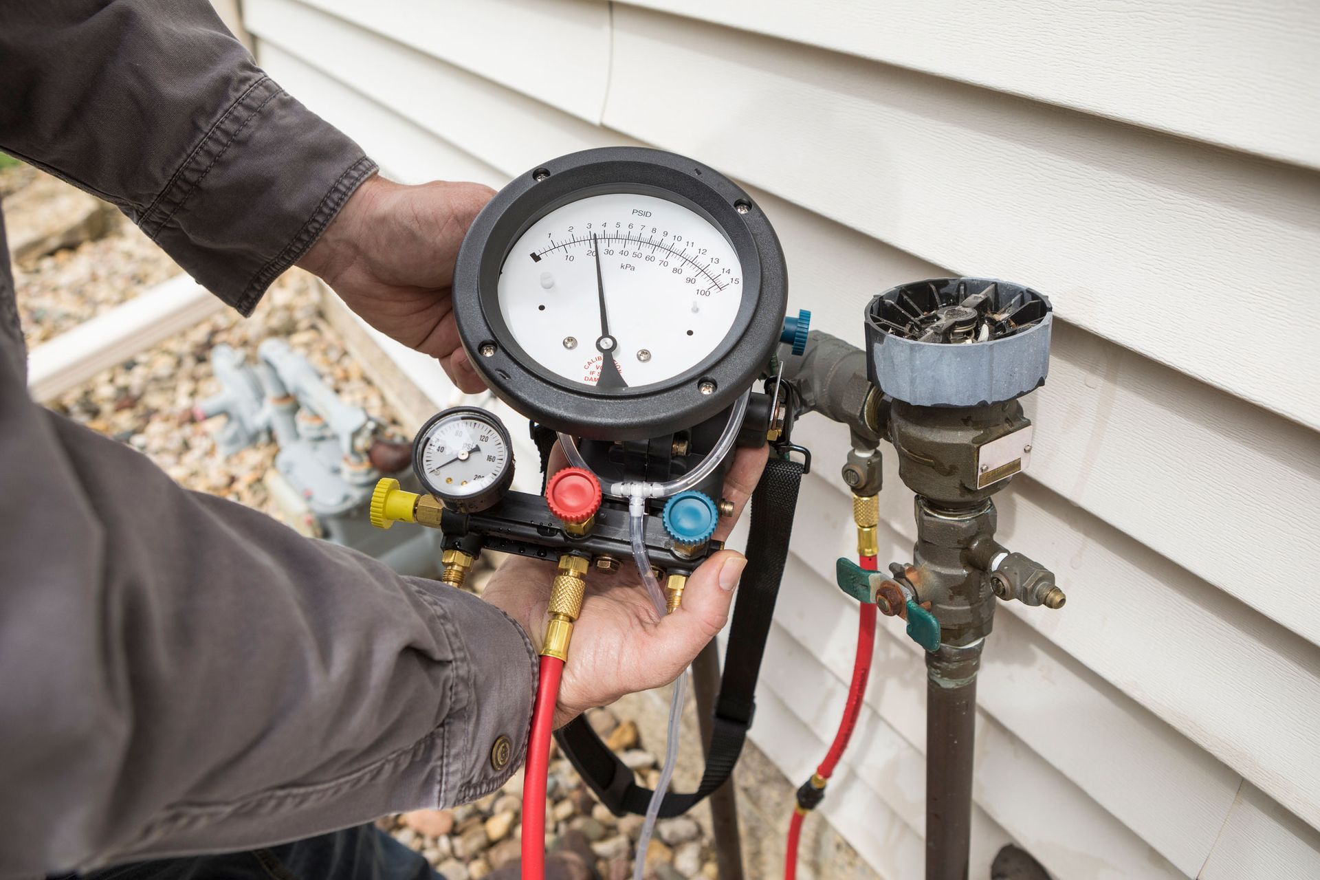 A man is holding a pressure gauge in front of a house.