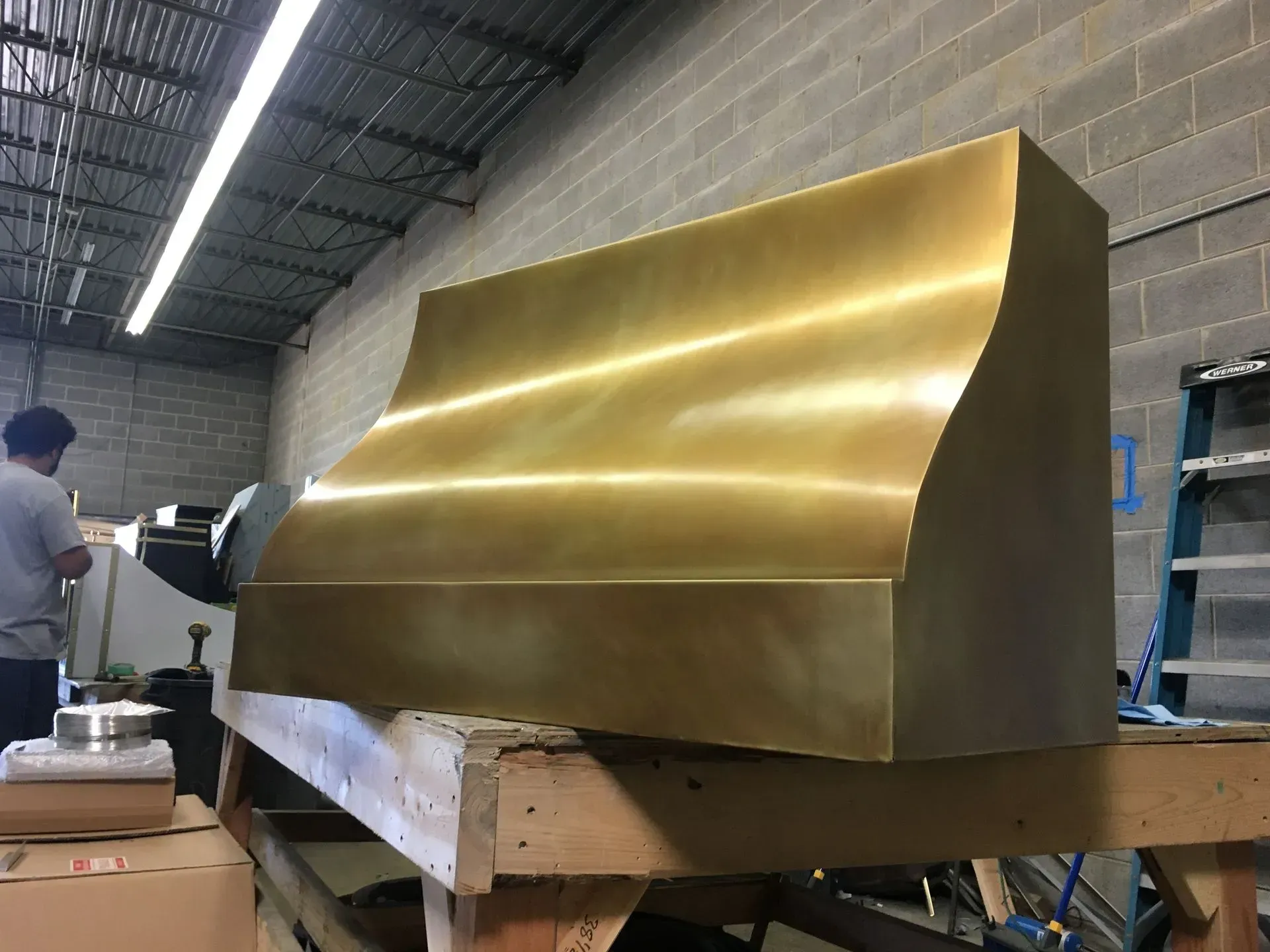 A man is working on a brass hood in a warehouse.