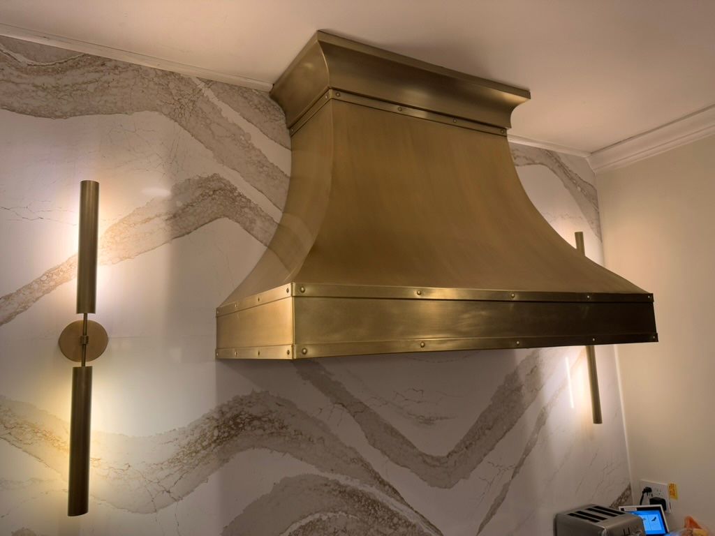 A brass hood is hanging from the ceiling in a kitchen.