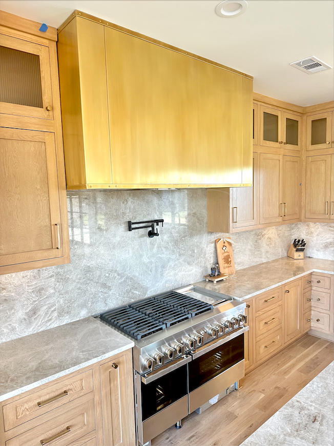A kitchen with wooden cabinets , a stove , and a brass hood.