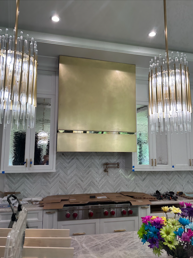 A kitchen with white cabinets and a brass hood