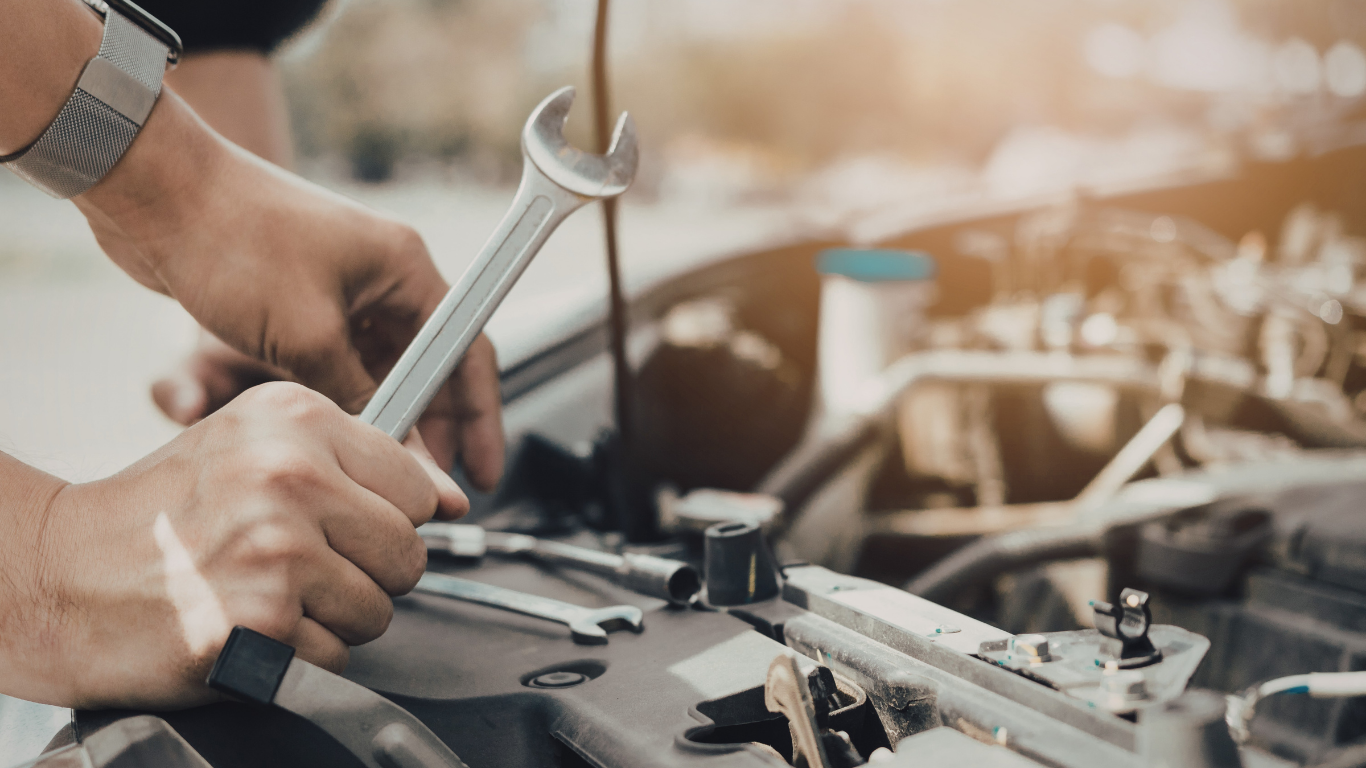 Hands using a wrench to repair a car engine in a garage