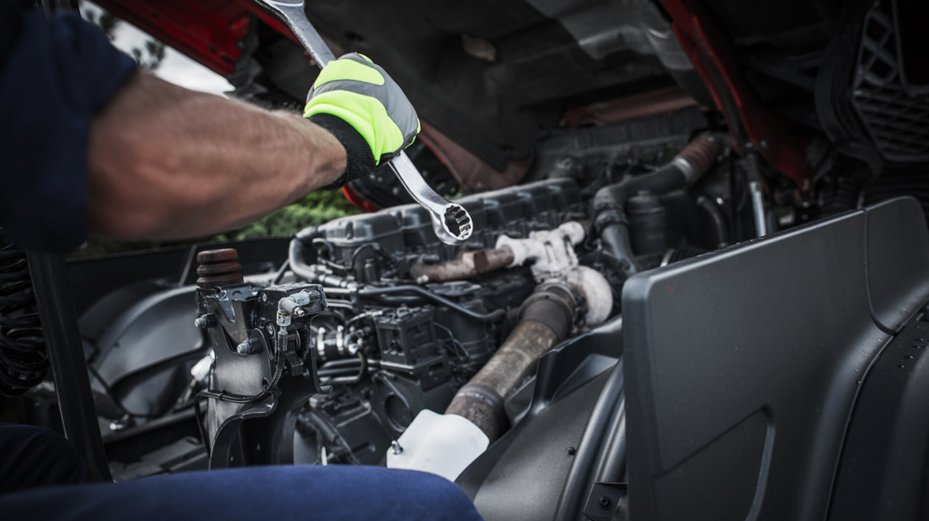 Mechanic working under a car hood, repairing engine components with tools.